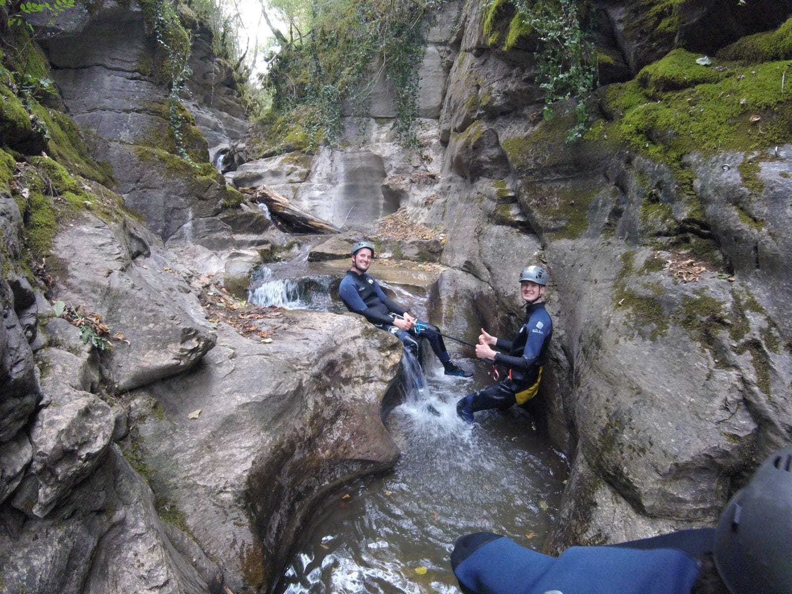 Two participants canyoning through a narrow rocky section with small cascades in Les Espones canyon