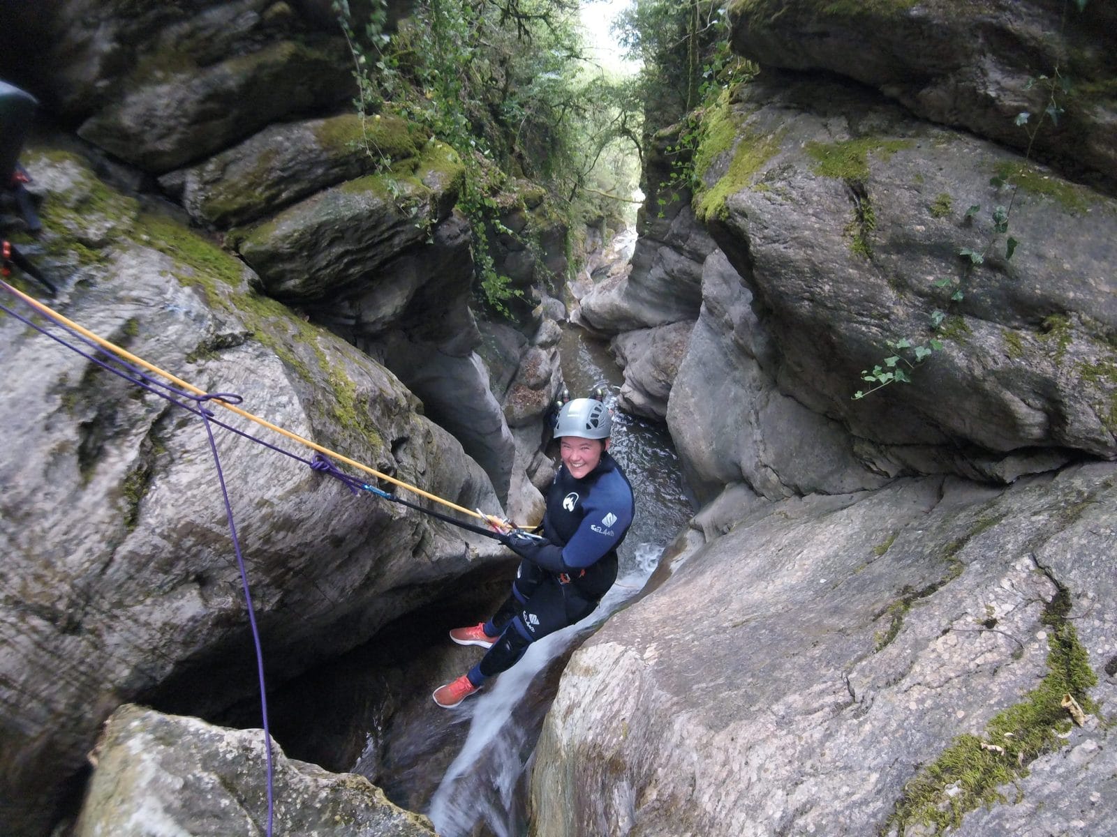 Participant rappelling down a narrow waterfall between steep rock walls in Les Espones canyon