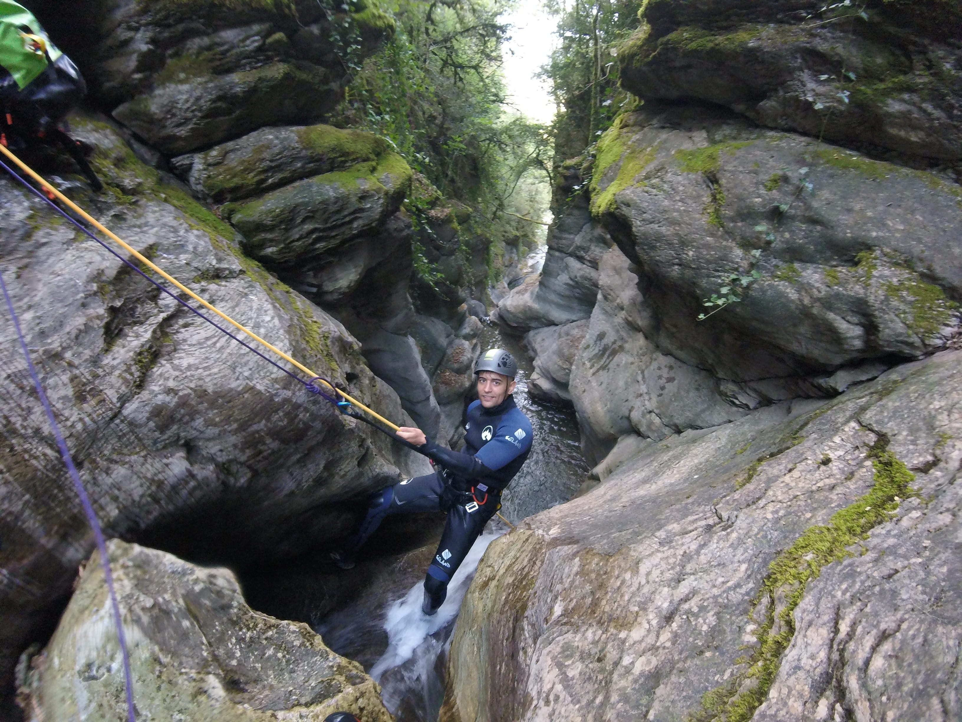 Participant rappelling down a narrow rocky section with flowing water in Les Espones canyon