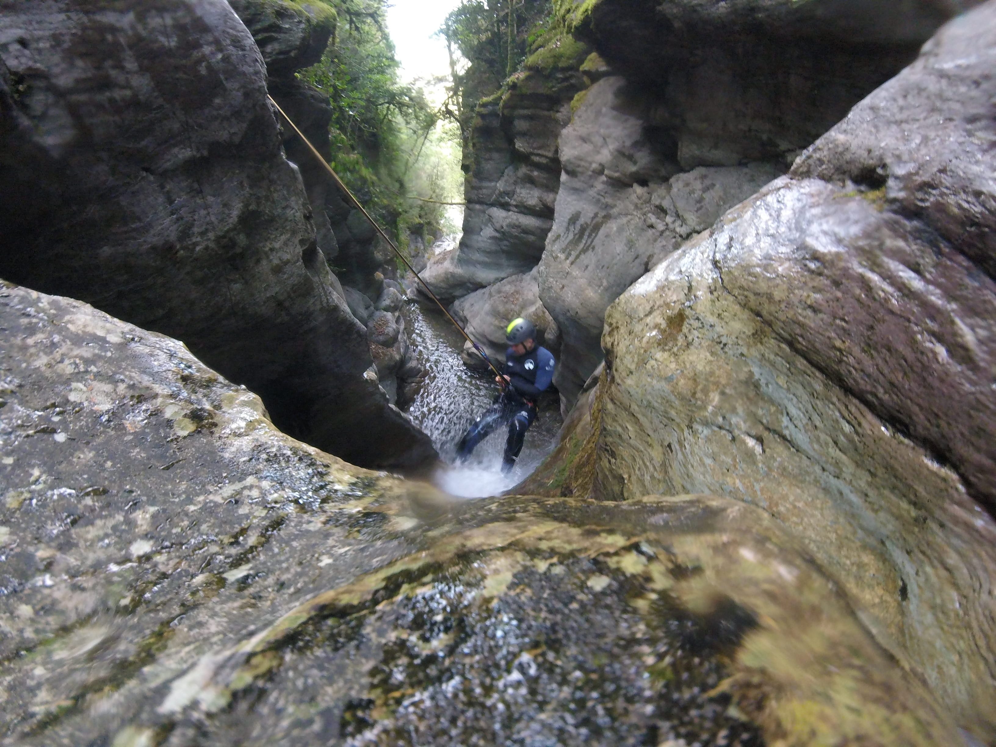 Participant rappelling through a narrow water-filled passage between rock walls in Les Espones canyon