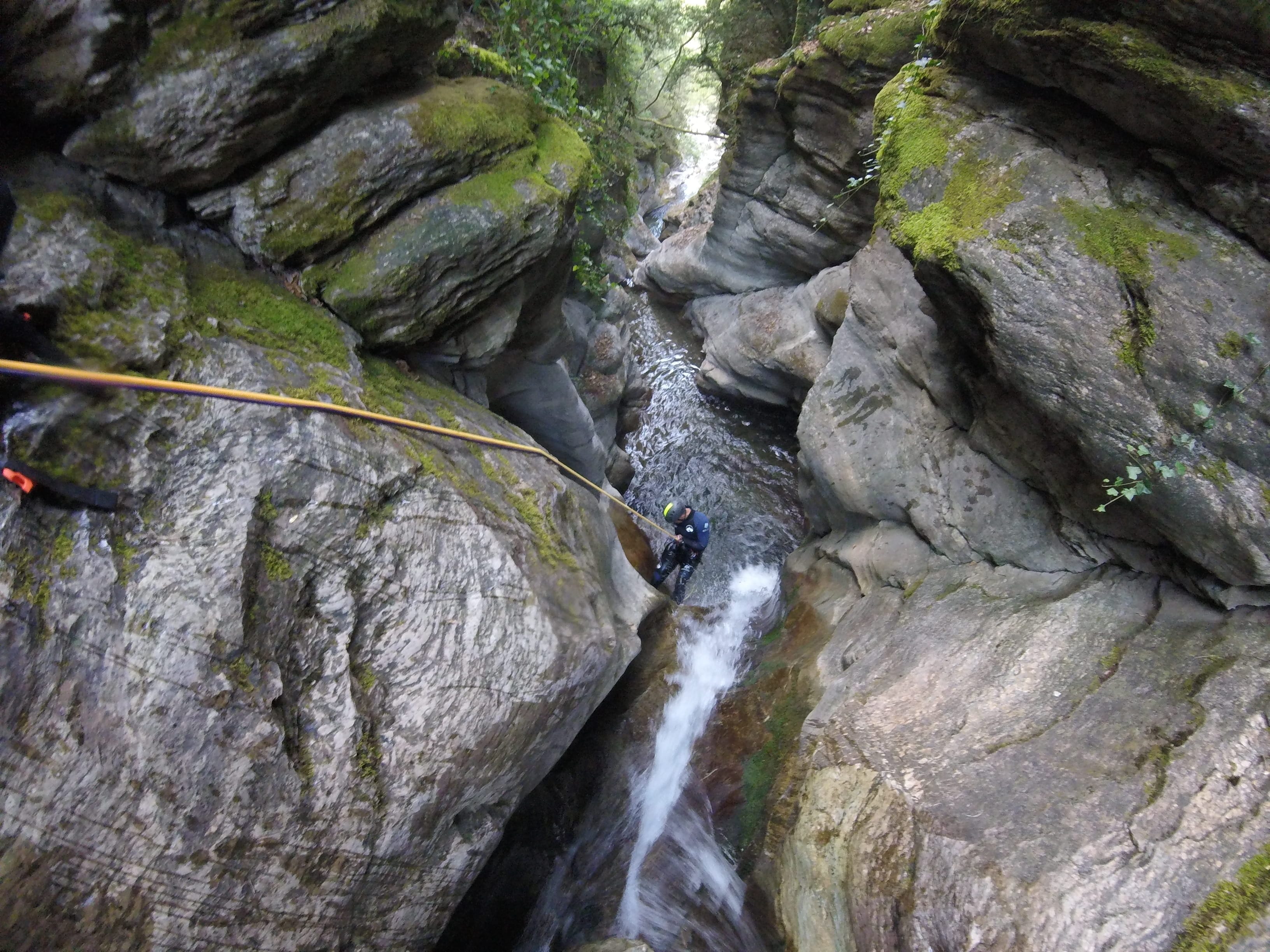Participant rappelling down a waterfall into a narrow rocky gorge in Les Espones canyon