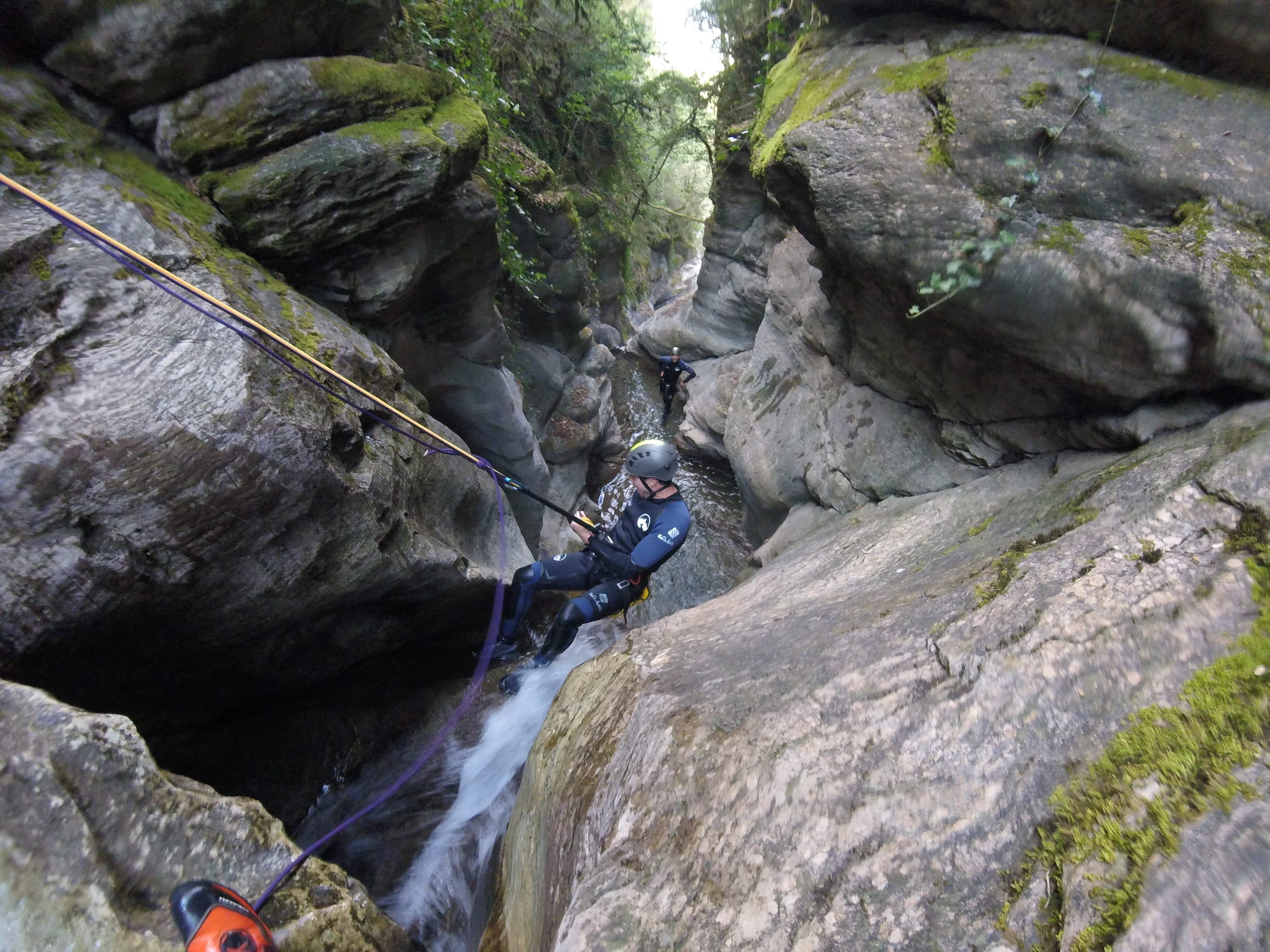 Participant rappelling beside a small waterfall through the narrow rocky gorge of Les Espones canyon