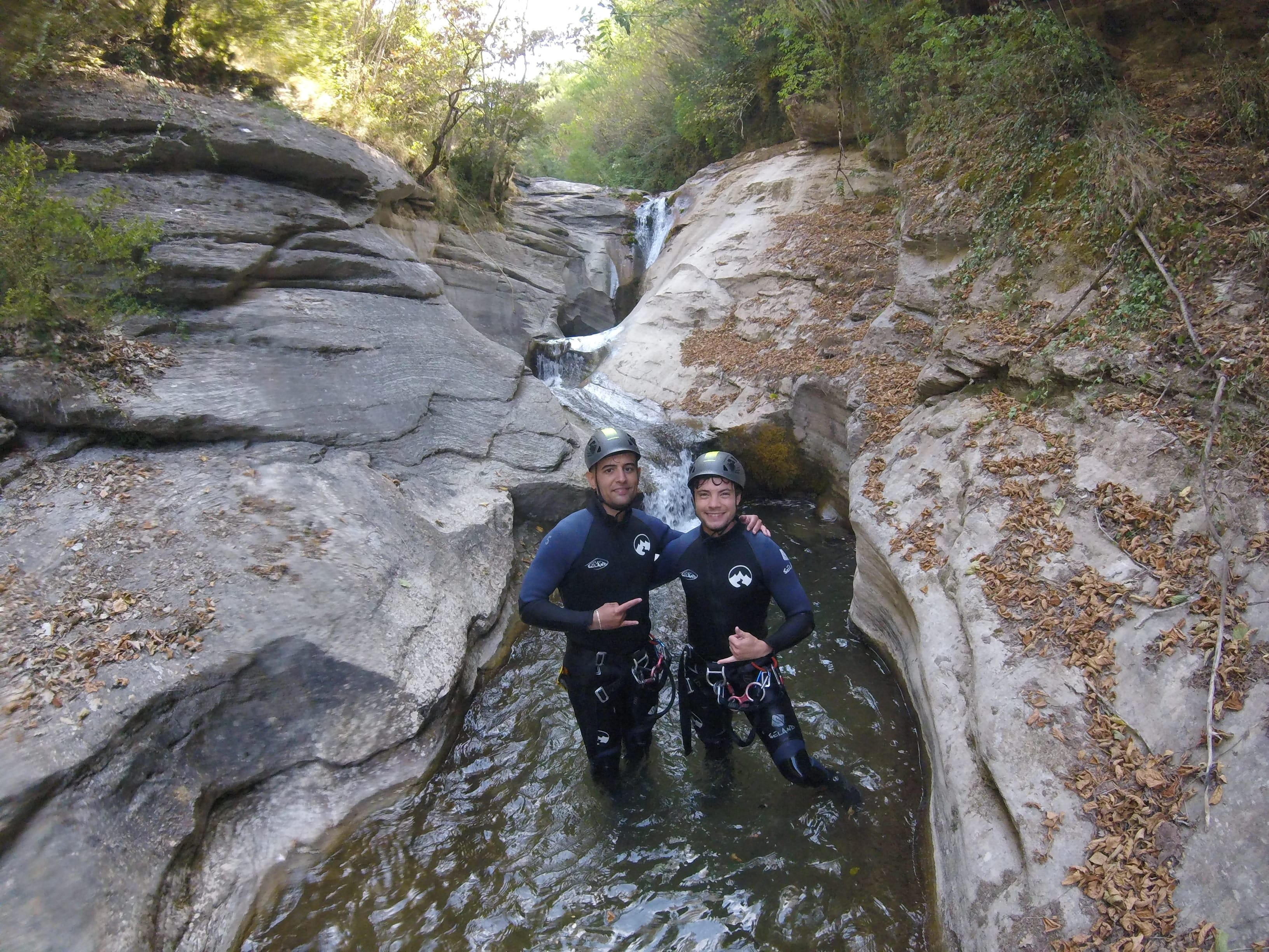 Two participants posing in a natural pool between smooth rock walls in Les Espones canyon