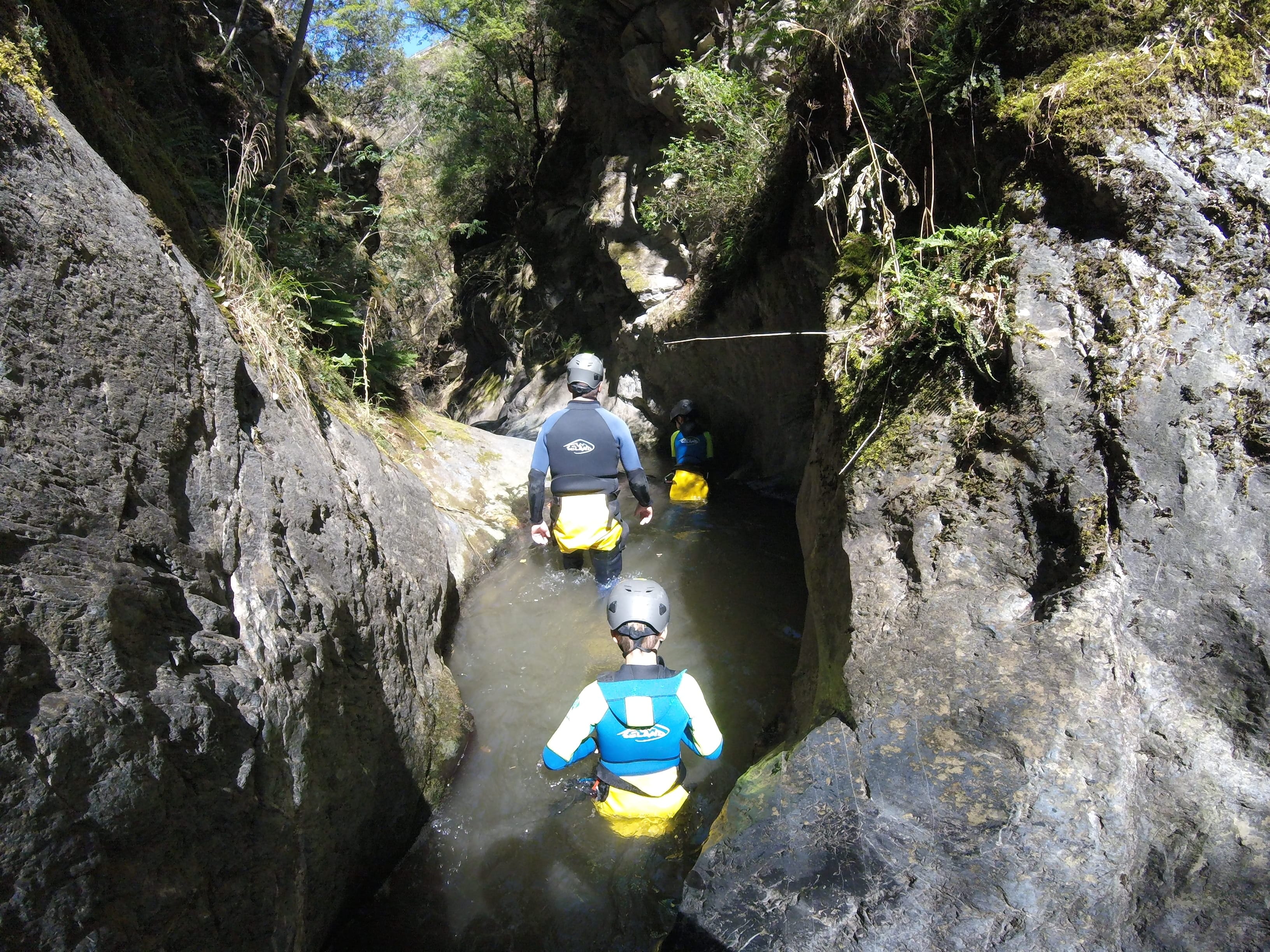 Participants walking through a narrow water-filled gorge between rock walls during a canyoning descent in Barranco de Berrós