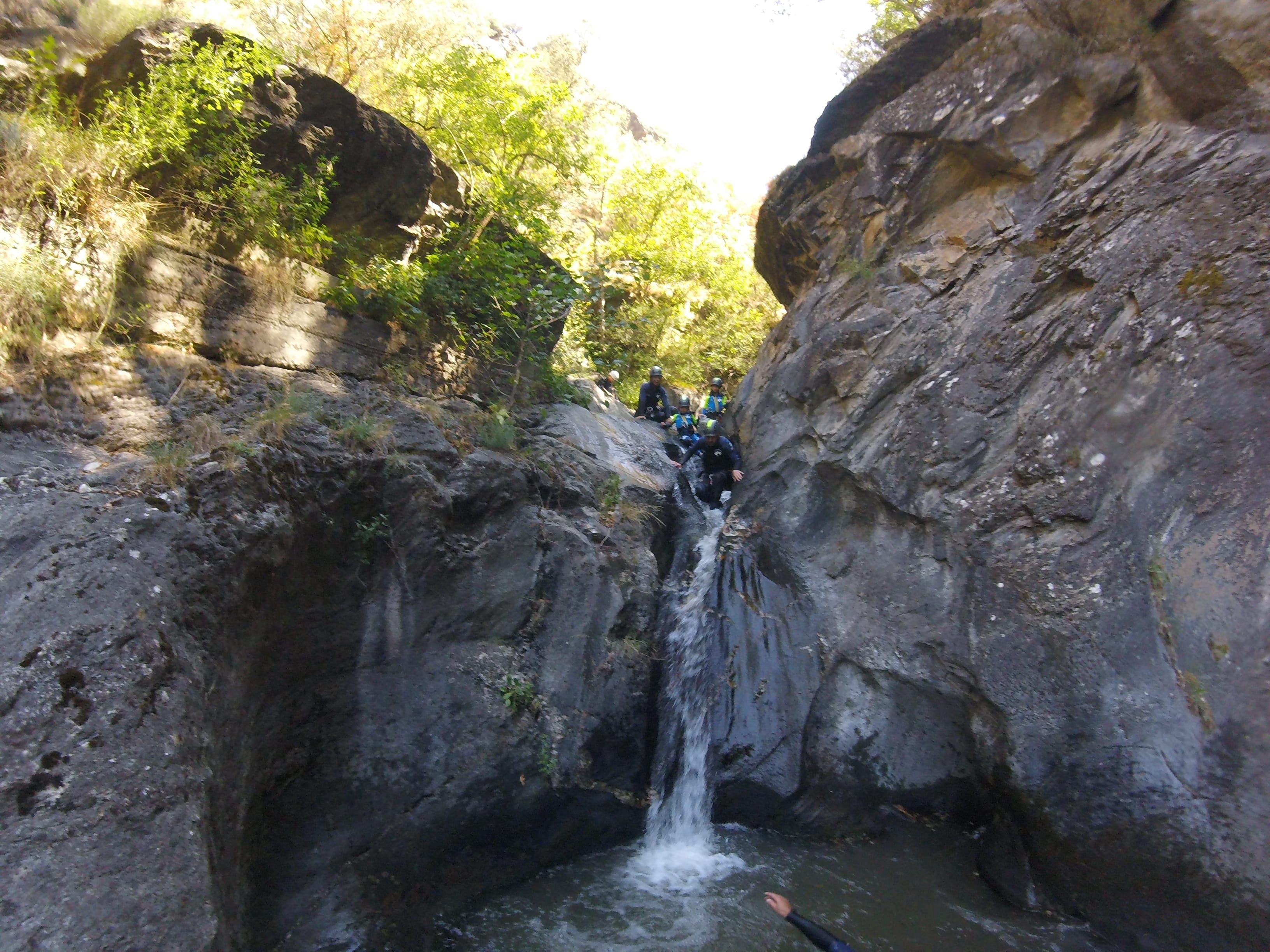 Participants descending a small waterfall between steep rock walls during a canyoning route in Barranco de Berrós