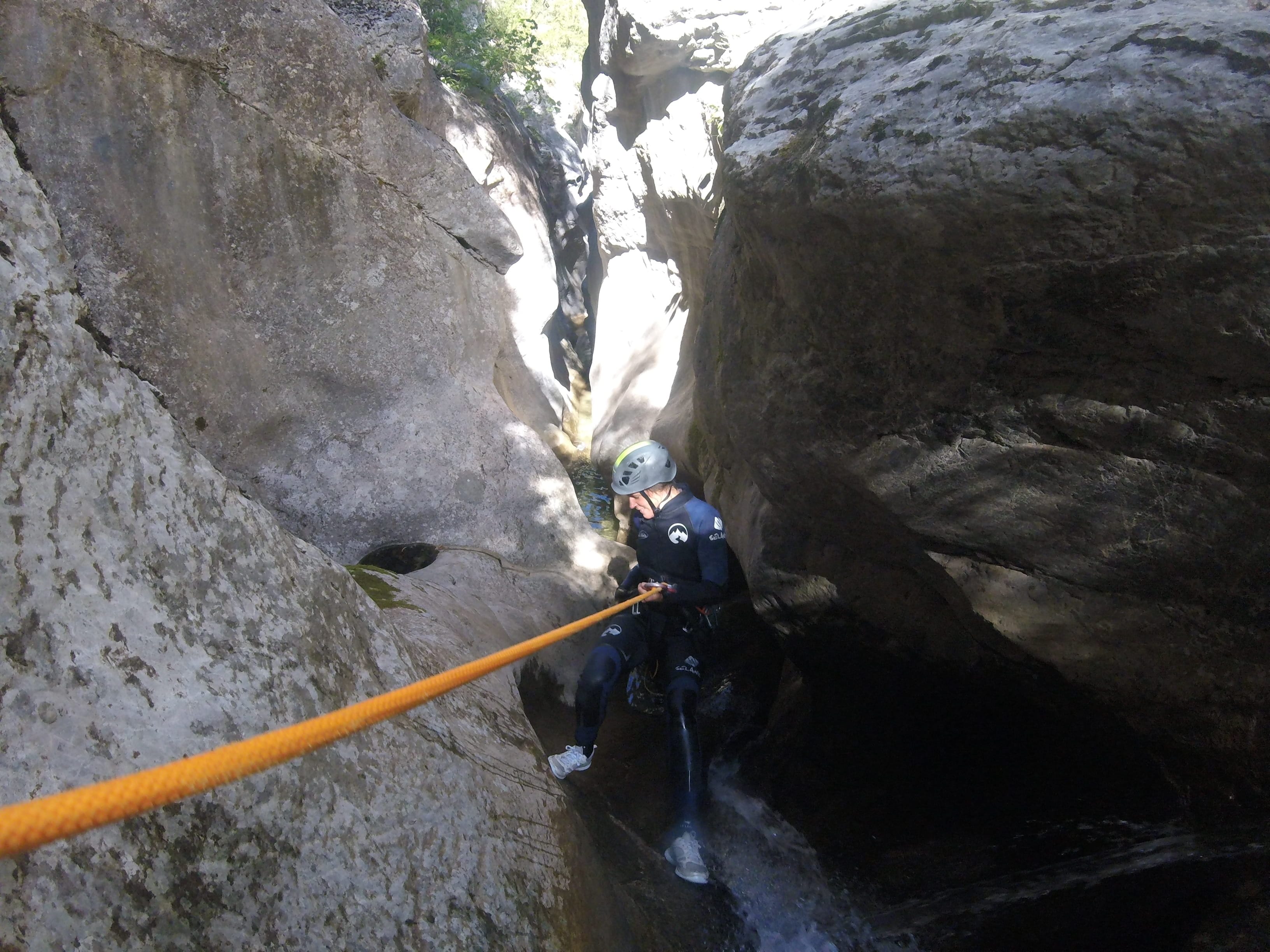 Canyoning participant descending on a rope through a narrow rocky passage in Barranc de Viu de Llevata