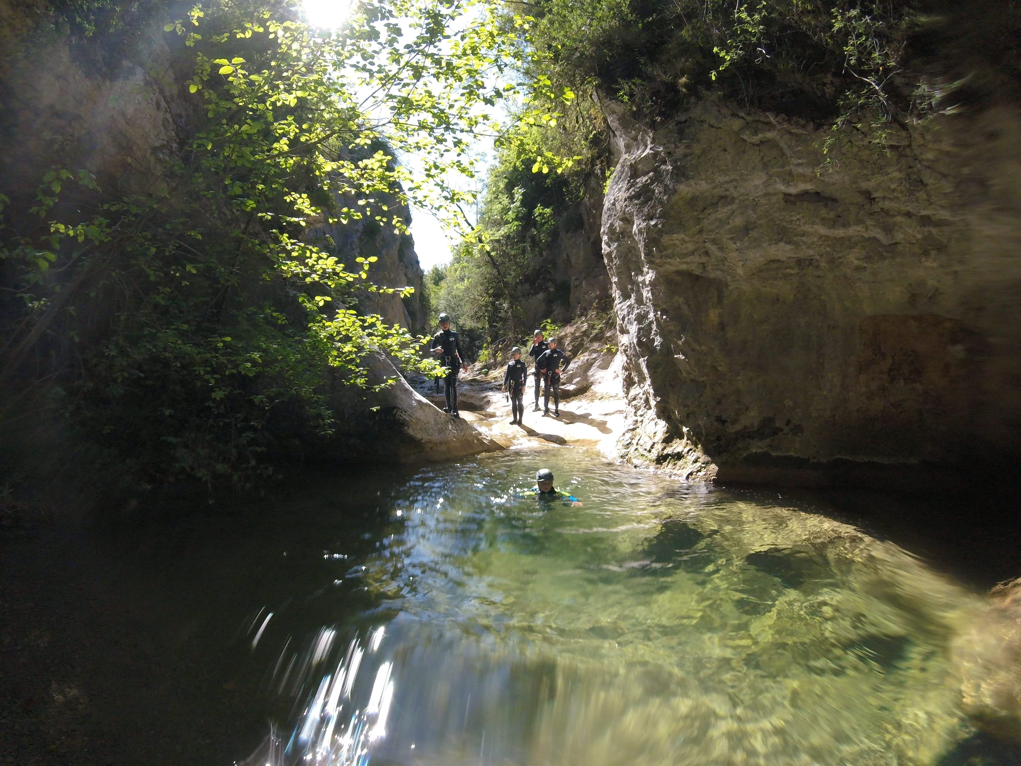 Canyoning group swimming and moving through a natural pool between rocky walls in Barranc de Viu de Llevata