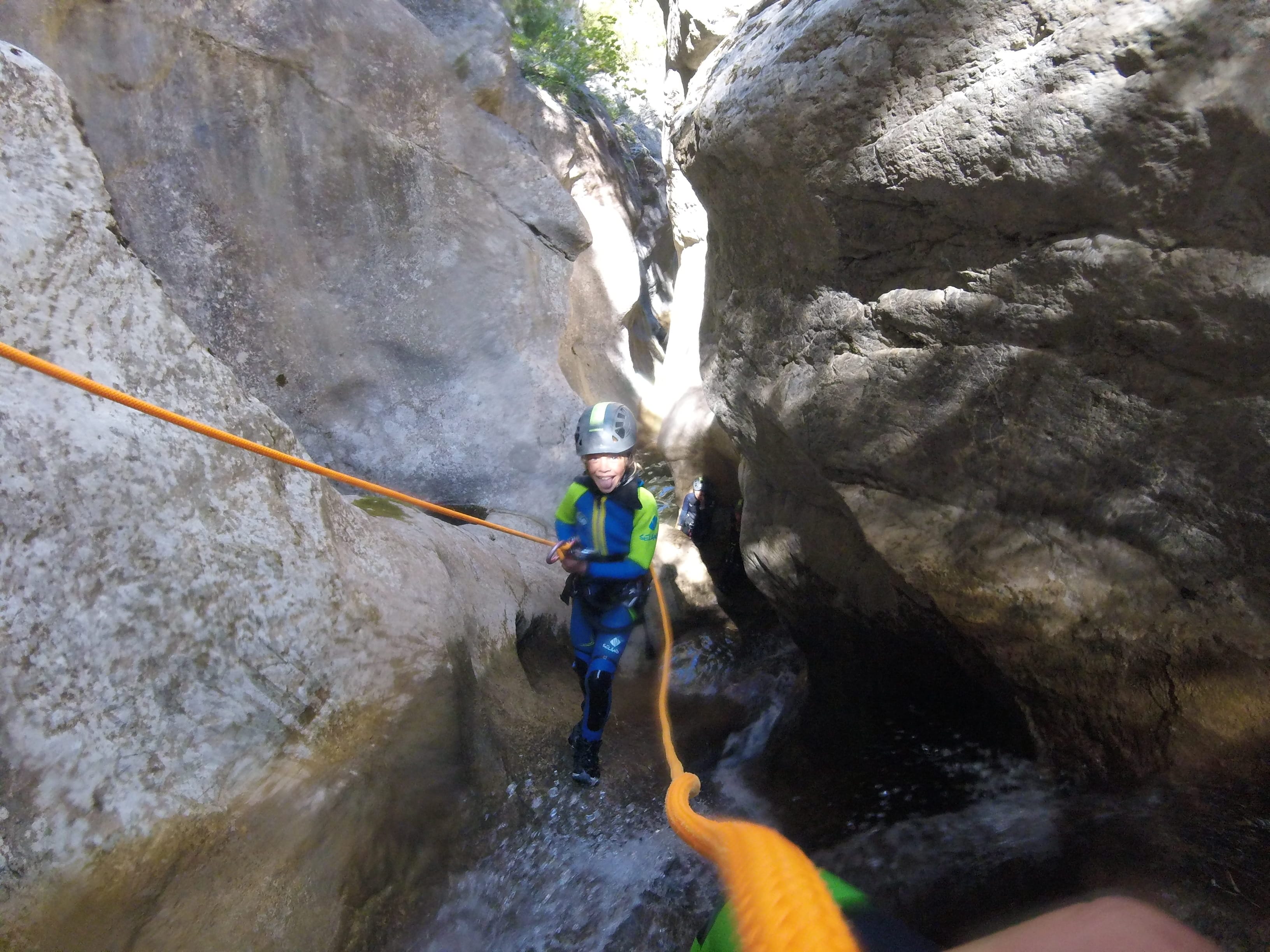 Young canyoning participant descending on a rope through a narrow rocky passage in Barranc de Viu de Llevata