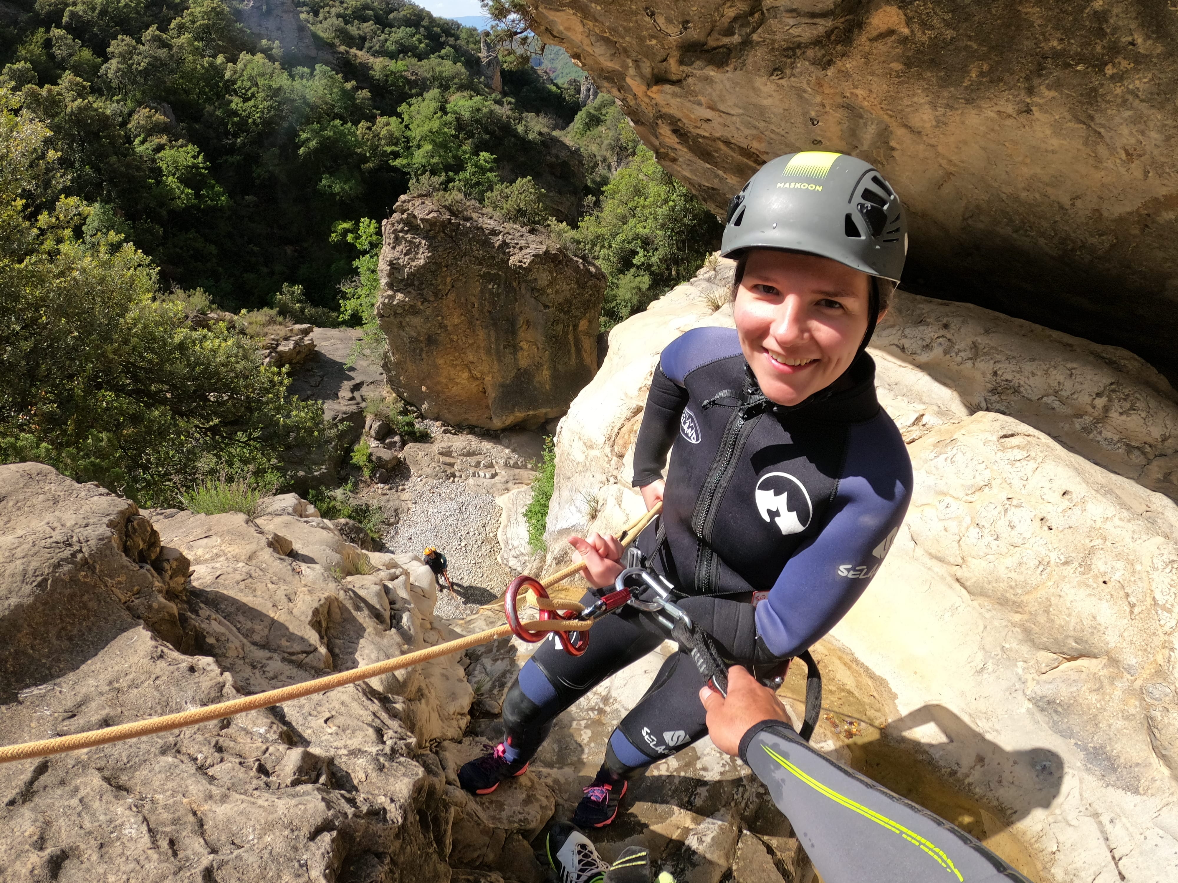 Participant smiling while preparing for a rappel descent in Barranco de Gurp, equipped with helmet, wetsuit and harness