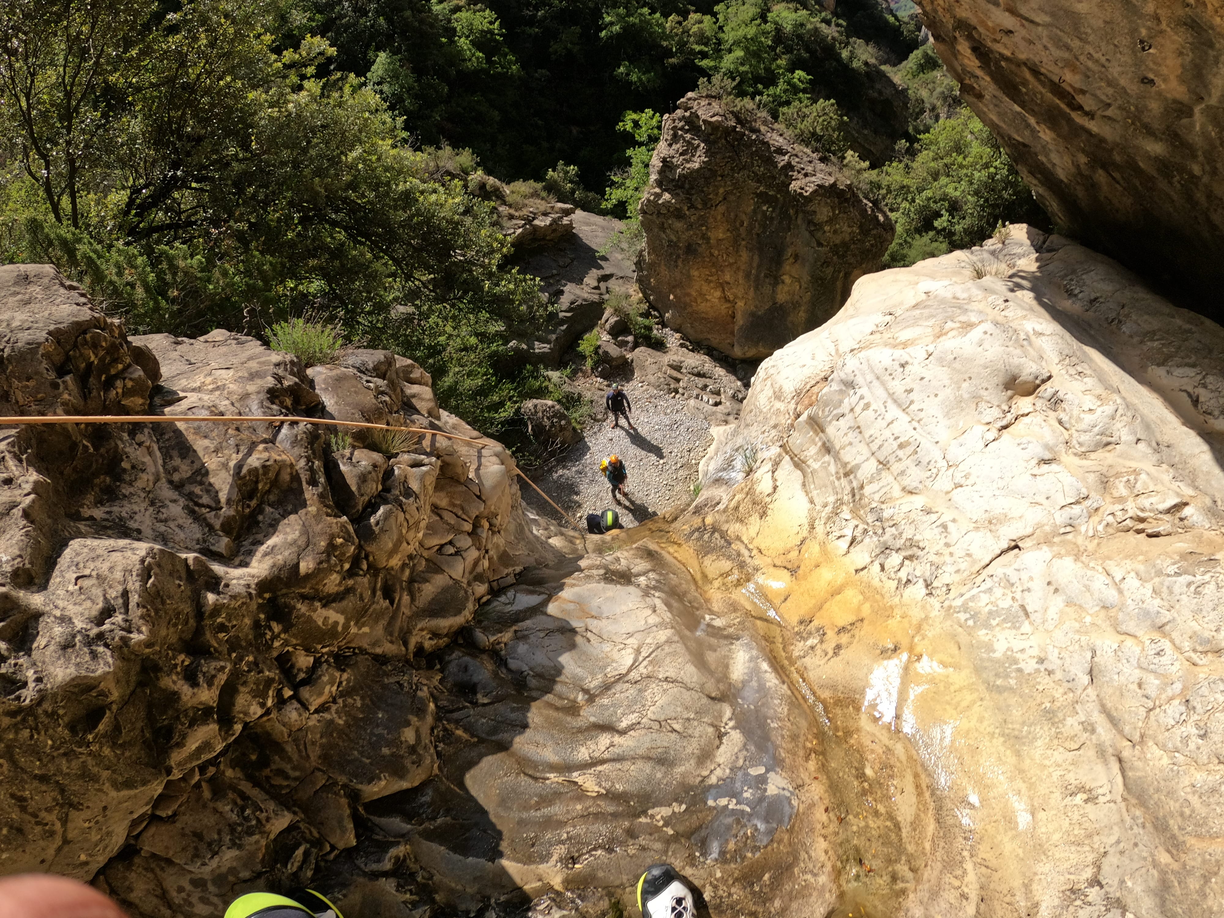 View from the top of a rappel descent down a rocky waterfall in Barranco de Gurp, with participants waiting below