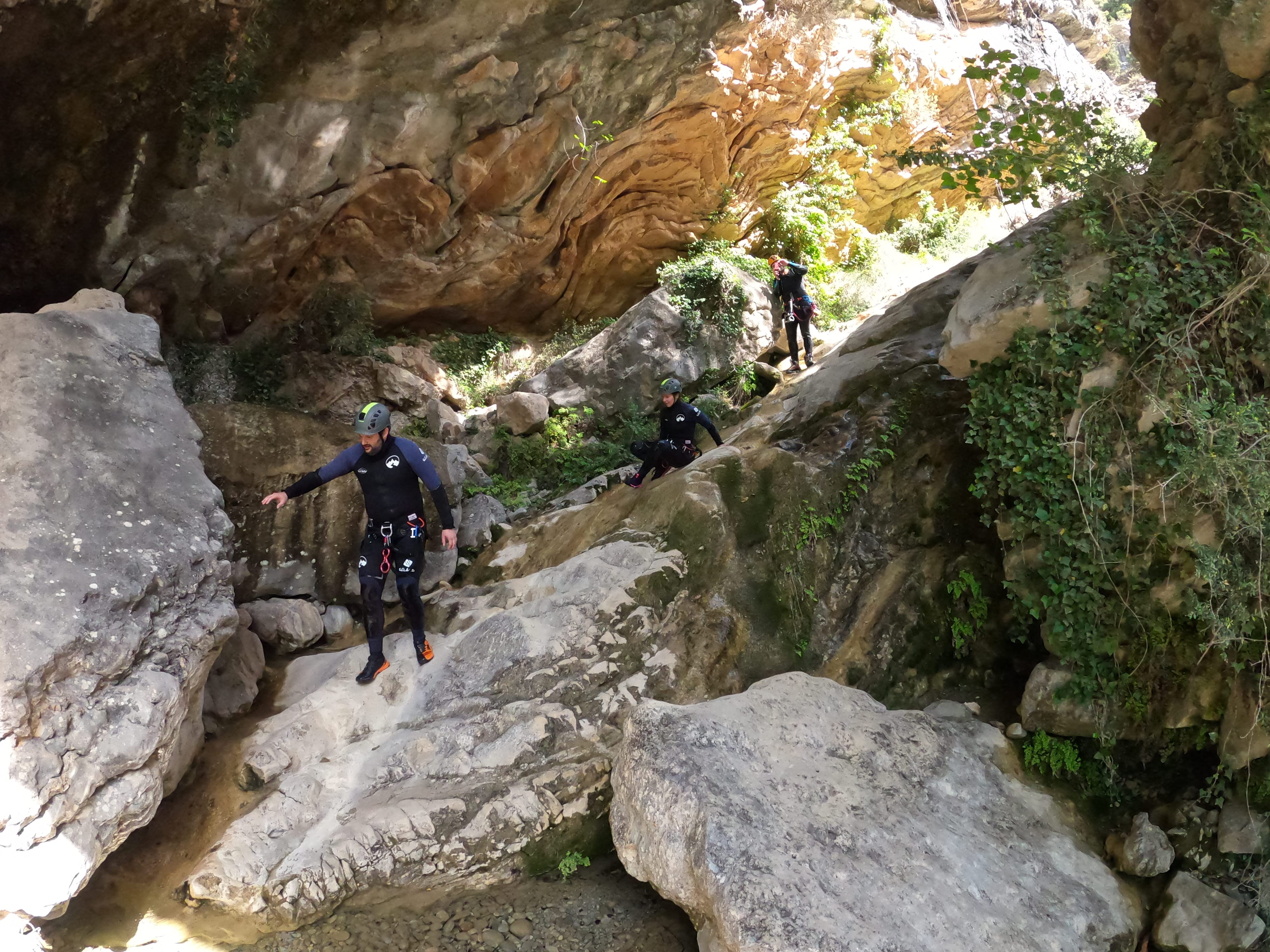 Participants descending through a rocky and shaded section of Barranco de Gurp surrounded by vegetation and large limestone formations