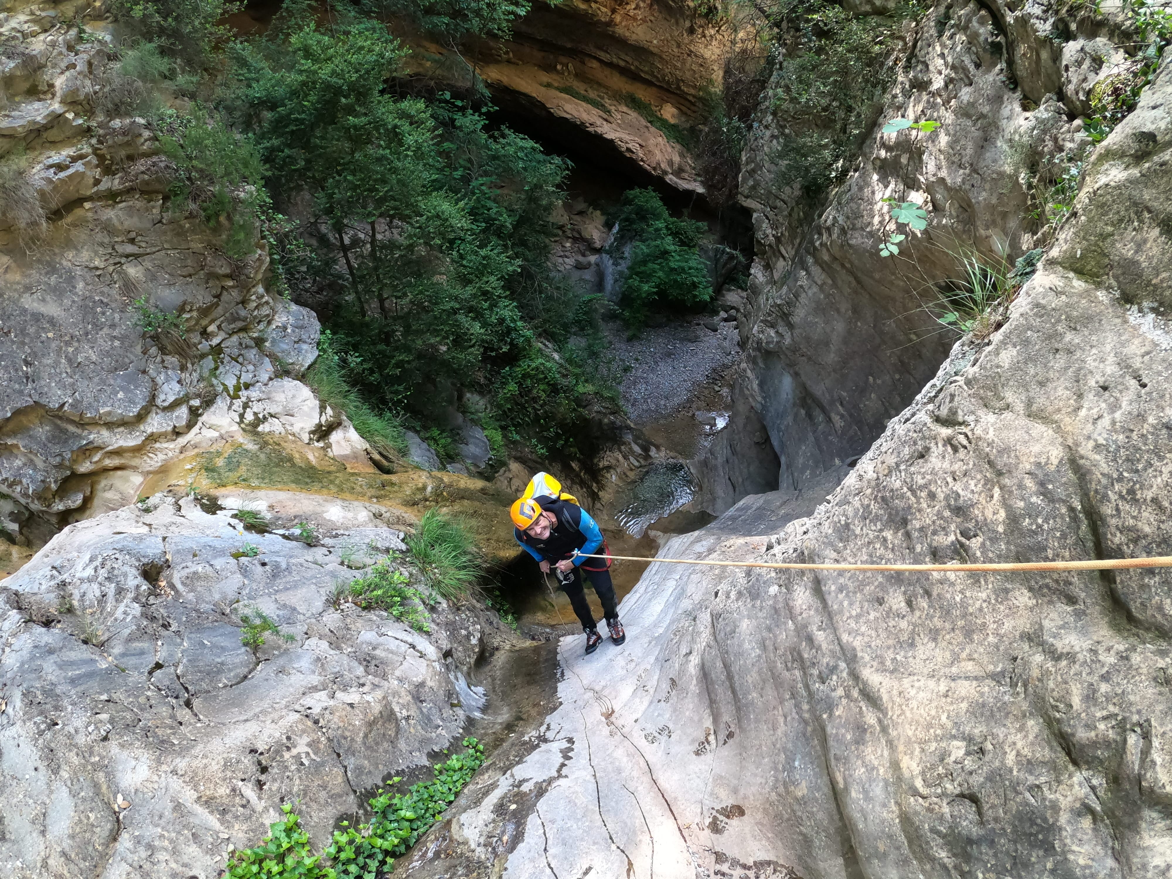 Participant rappelling down a smooth limestone wall into a deep, wooded section of Barranco de Gurp