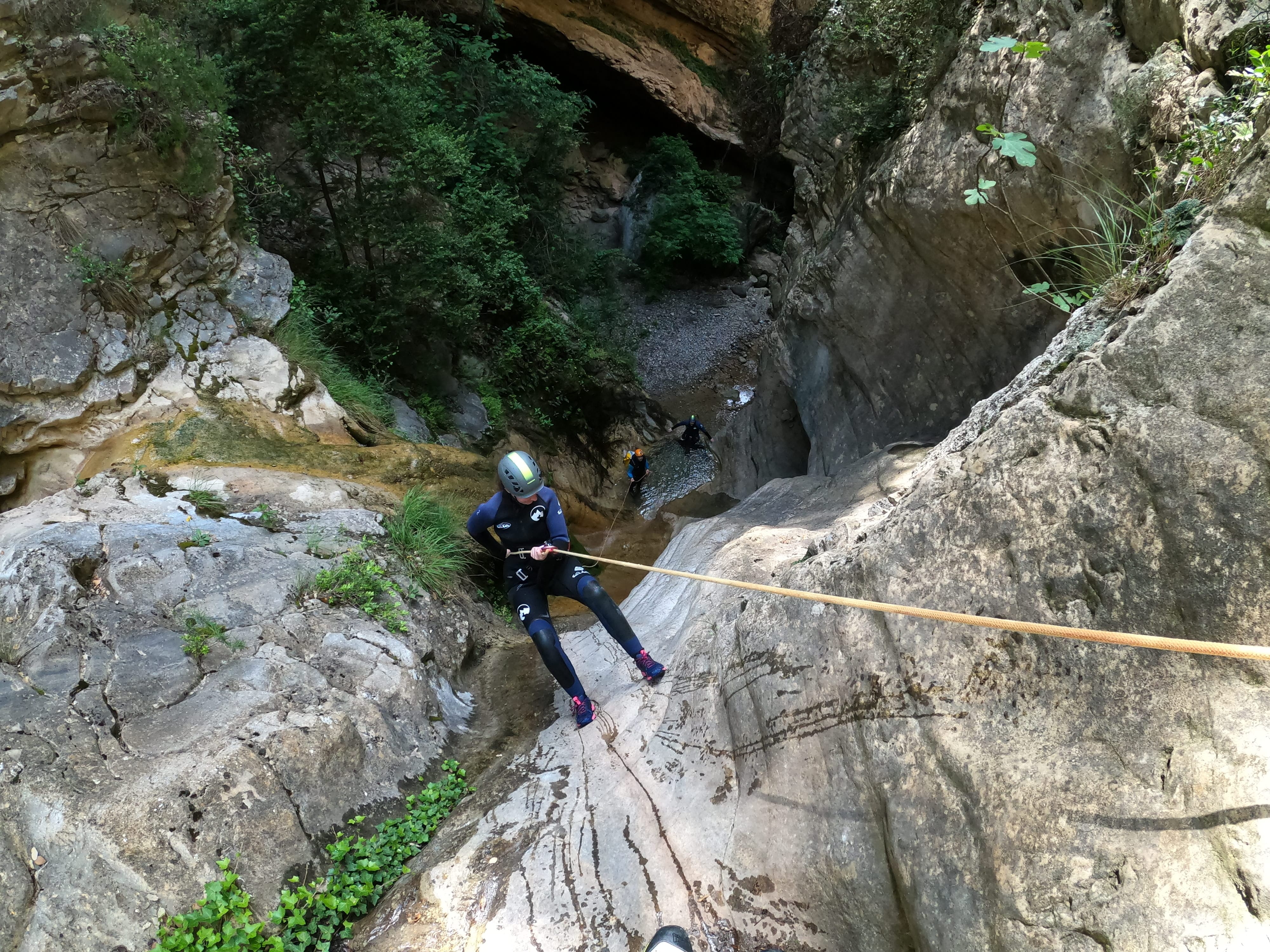 Participant rappelling down a steep limestone chute in Barranco de Gurp, with other canyoners waiting below