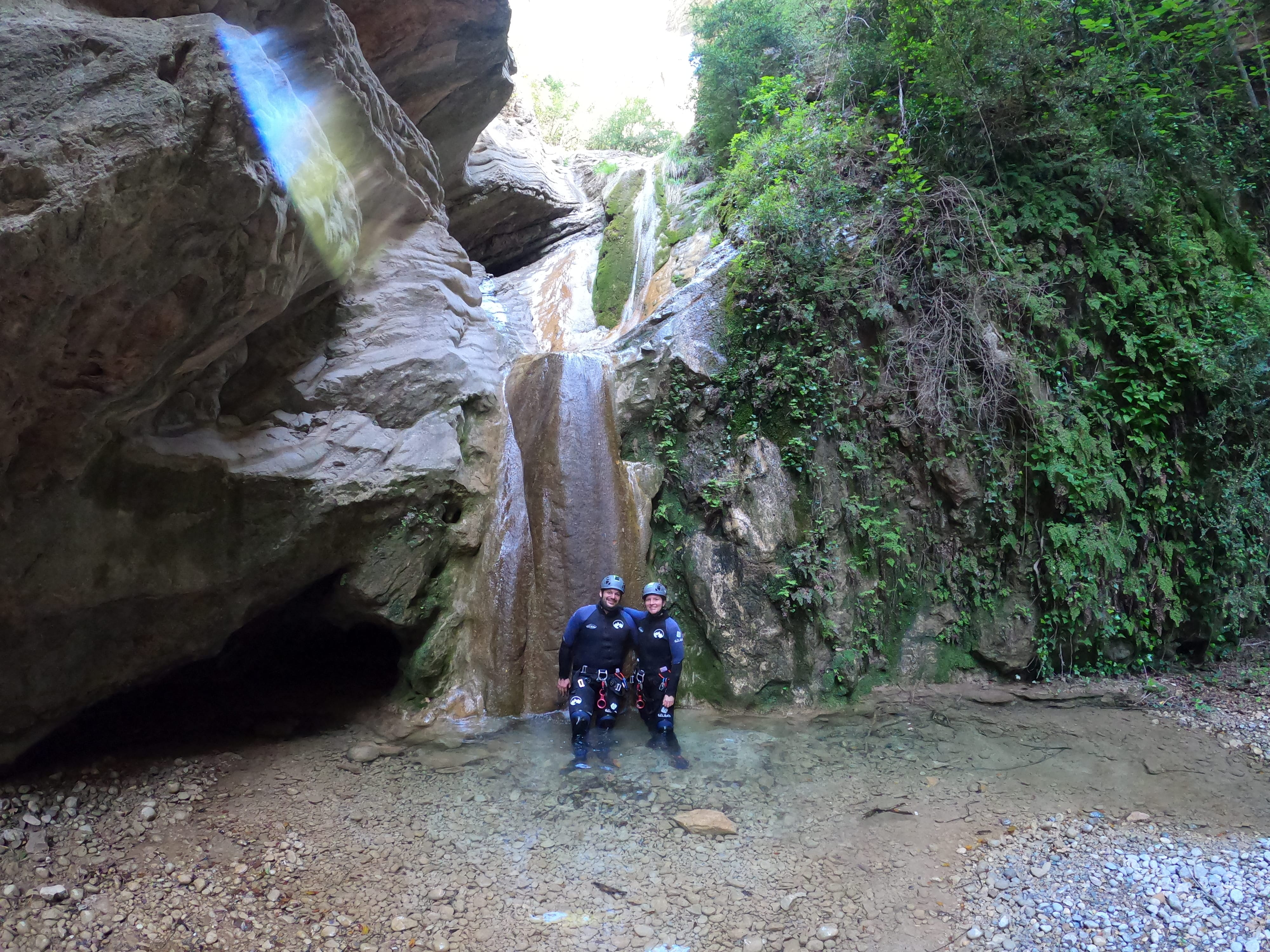 Two participants posing at the foot of a small waterfall surrounded by lush vegetation in Barranco de Gurp