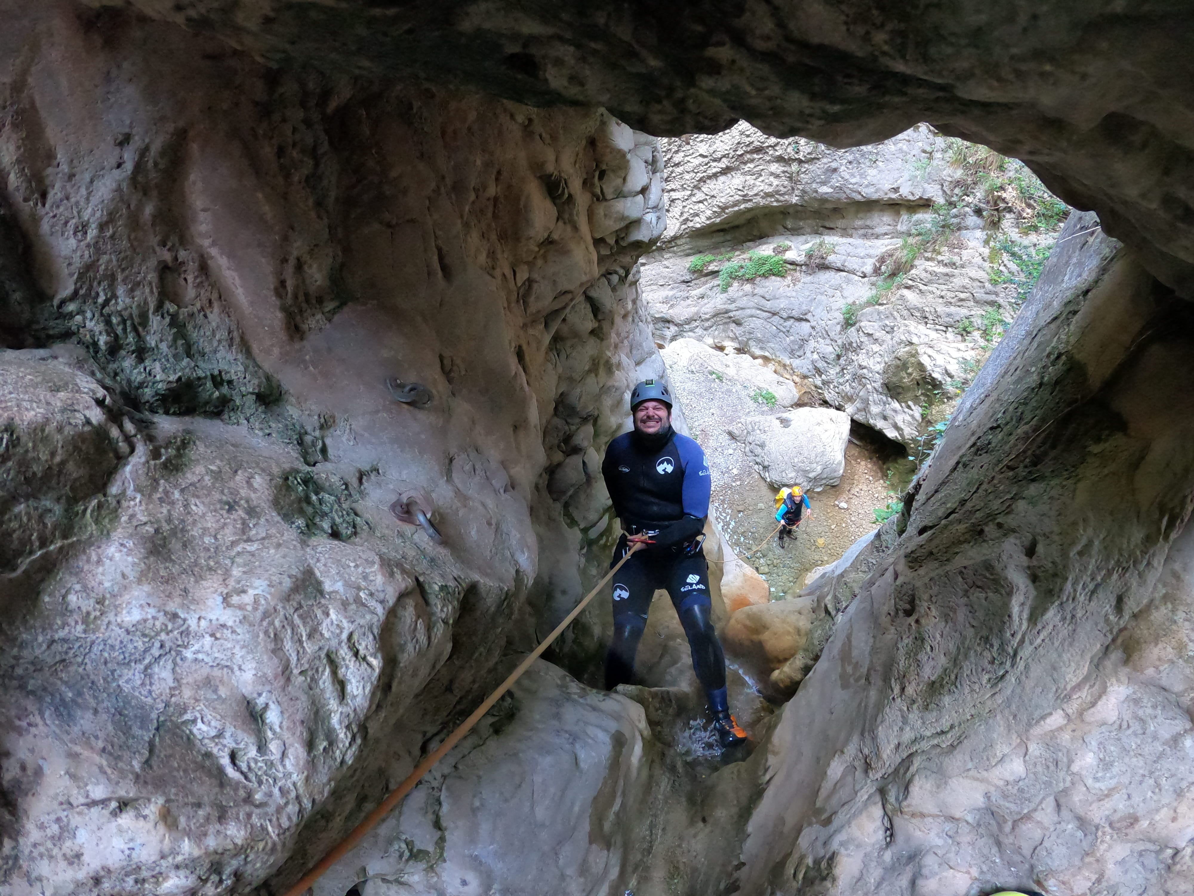 Participant rappelling through a narrow rock passage in Barranco de Gurp, with another canyoner waiting below
