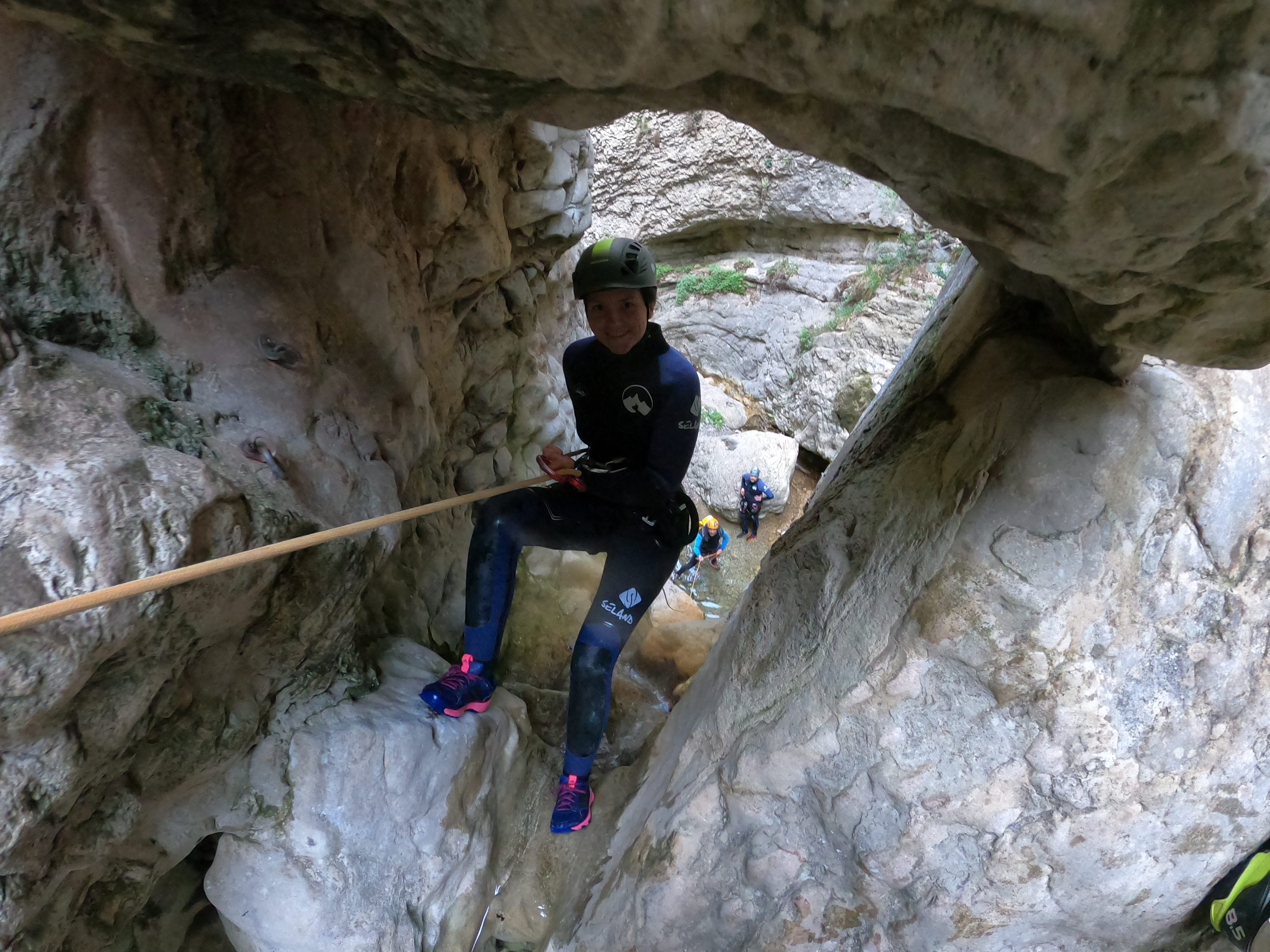 Participant rappelling through a narrow sculpted rock passage in Barranco de Gurp, with other canyoners visible below