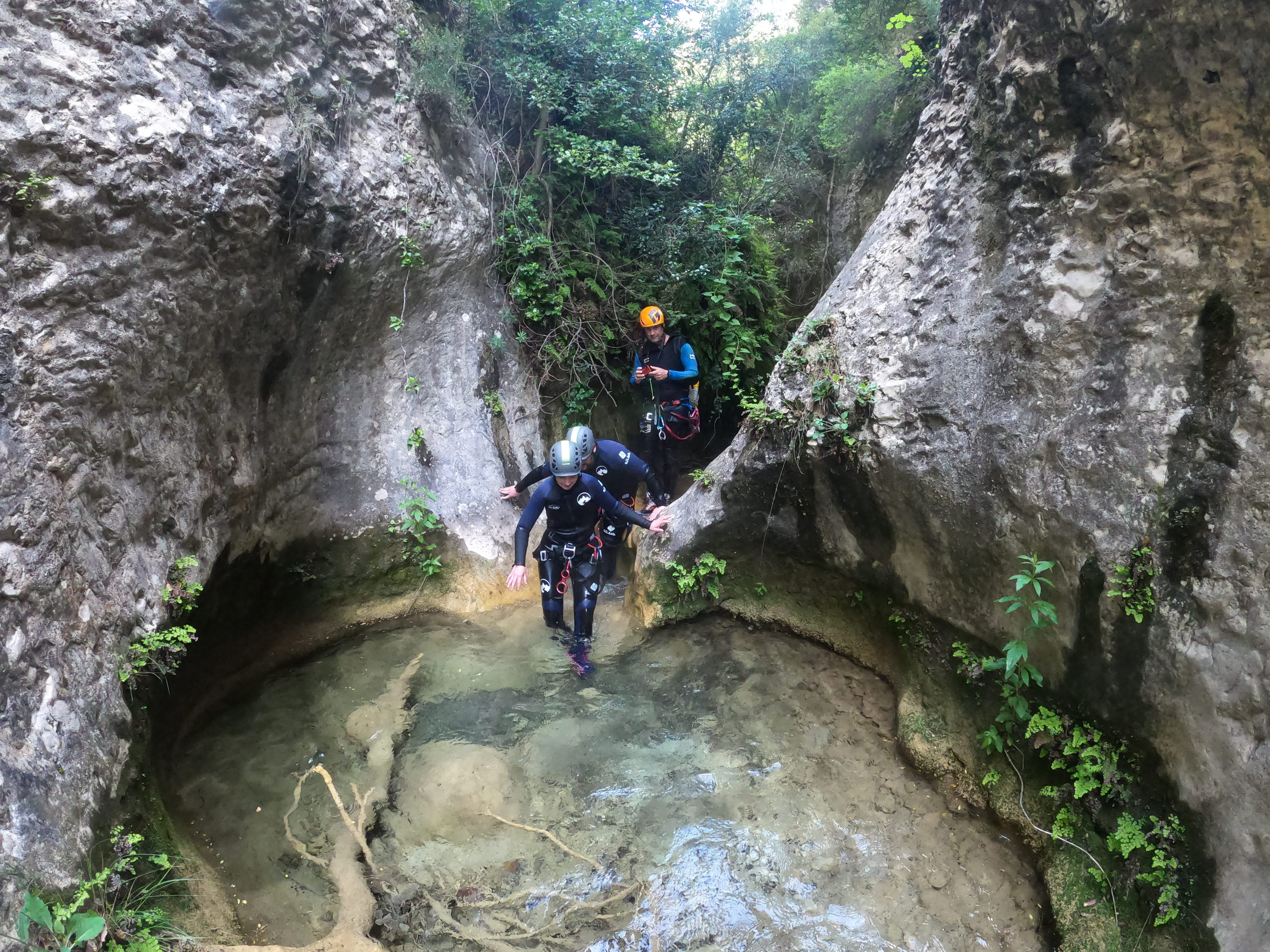 Participants walking through a shallow natural pool between narrow limestone walls in Barranco de Gurp