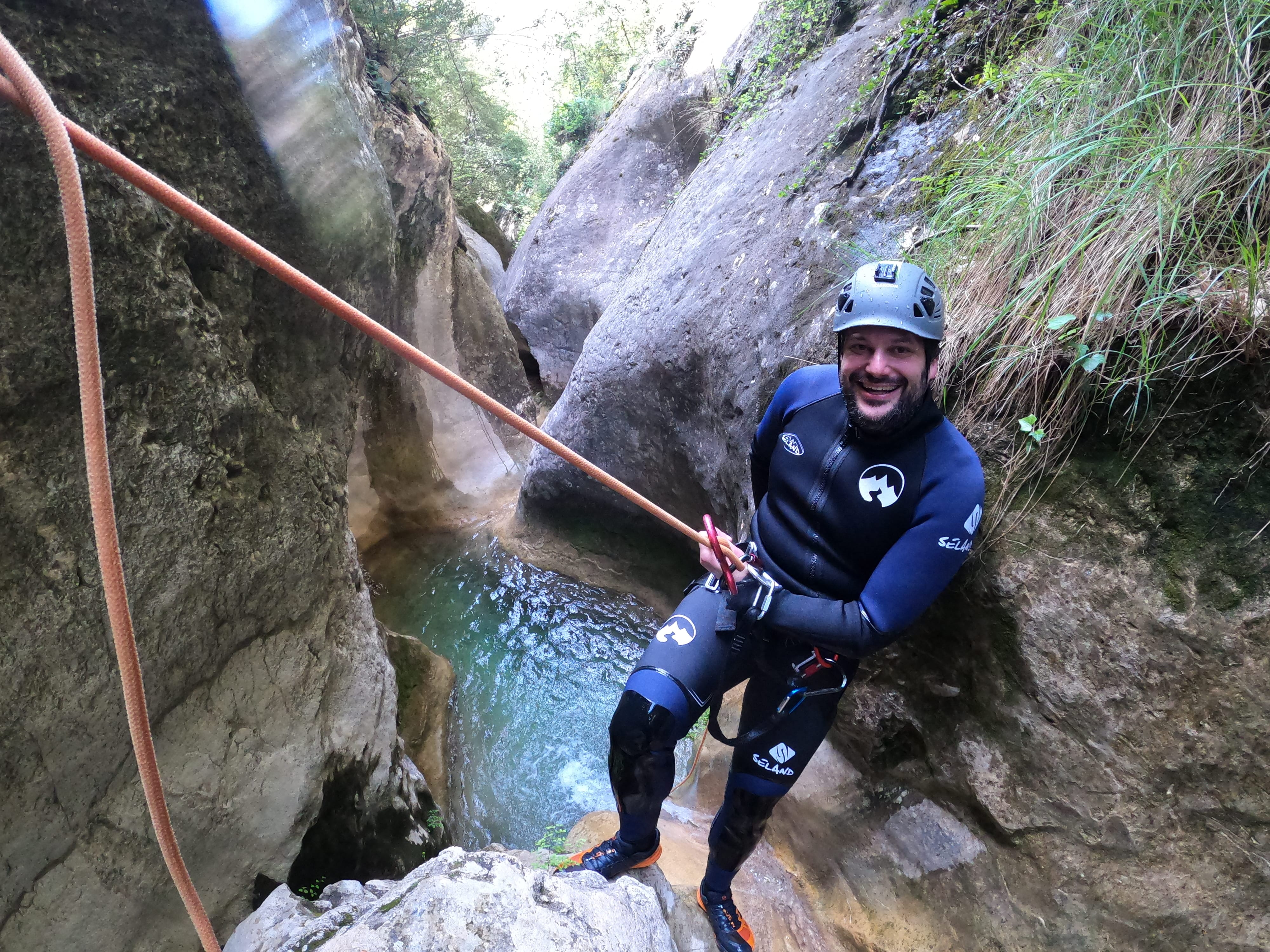 Smiling participant preparing to rappel beside a clear natural pool in a narrow section of Barranco de Gurp