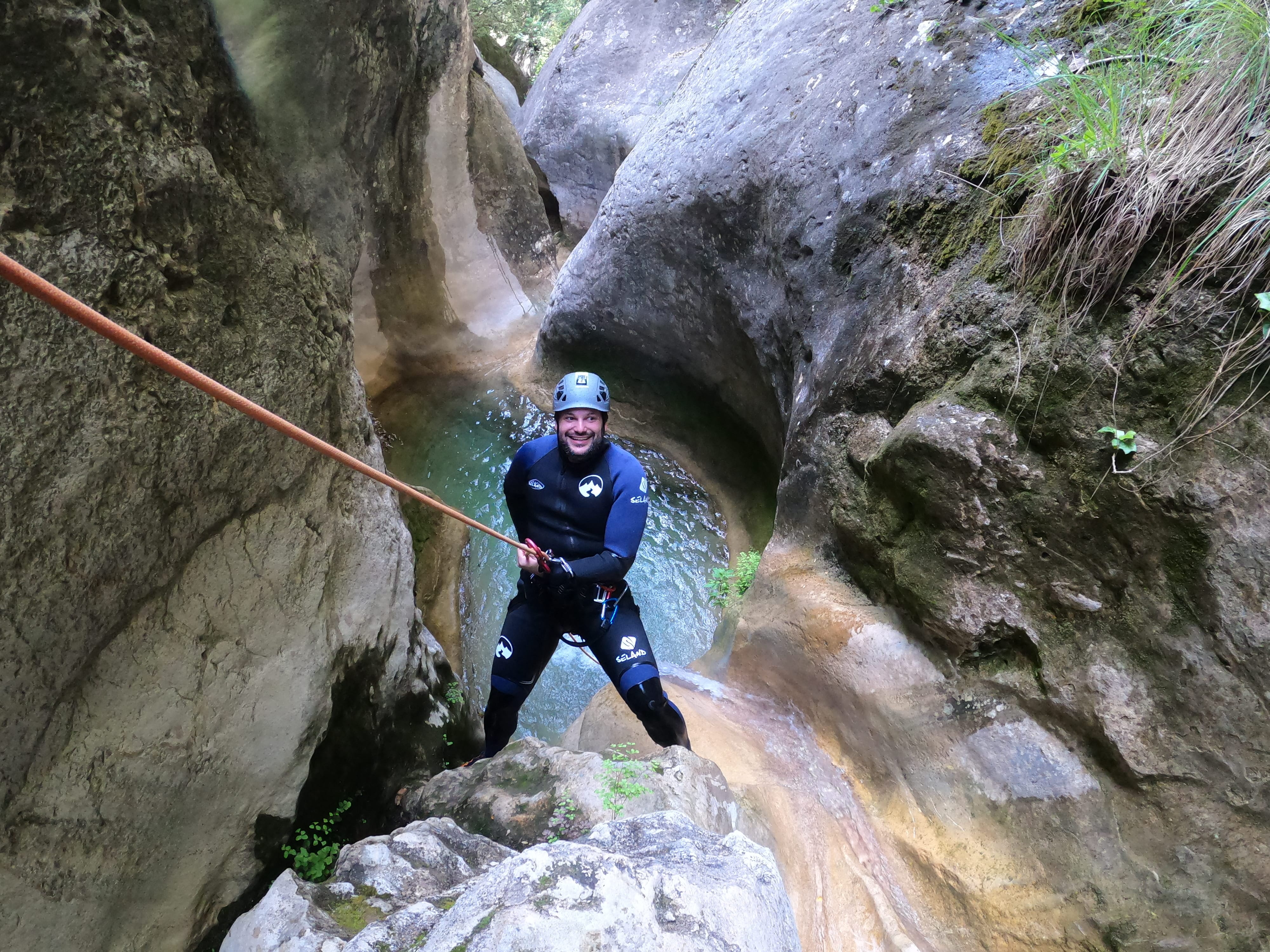 Smiling participant rappelling above a clear natural pool between narrow rock walls in Barranco de Gurp