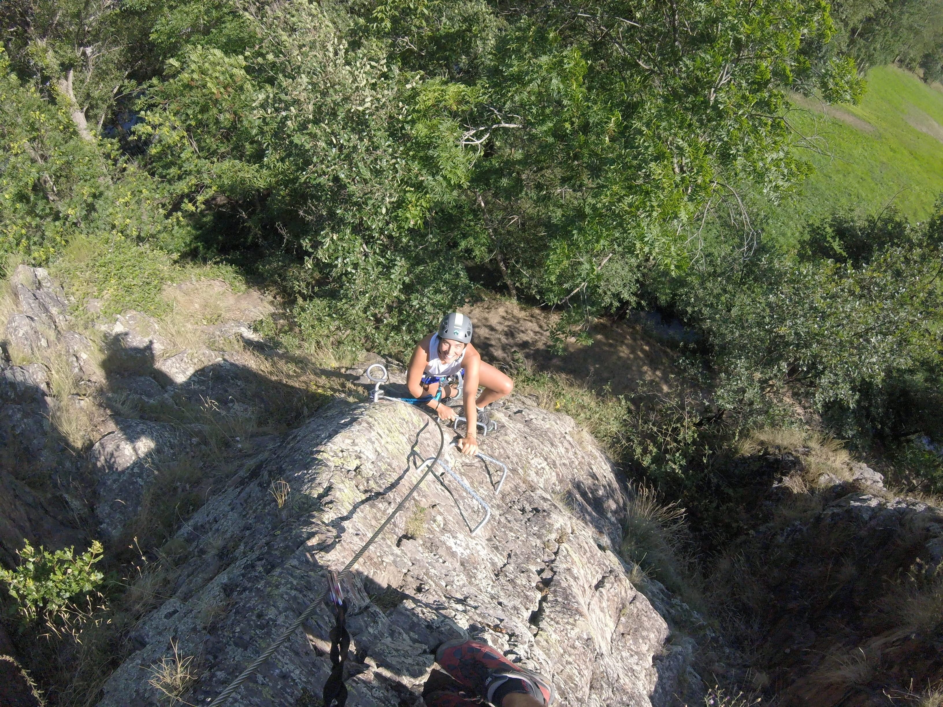 Participante subiendo por un tramo rocoso y empinado de la vía ferrata Salt de Botanal utilizando grapas metálicas y asegurada al cable de seguridad