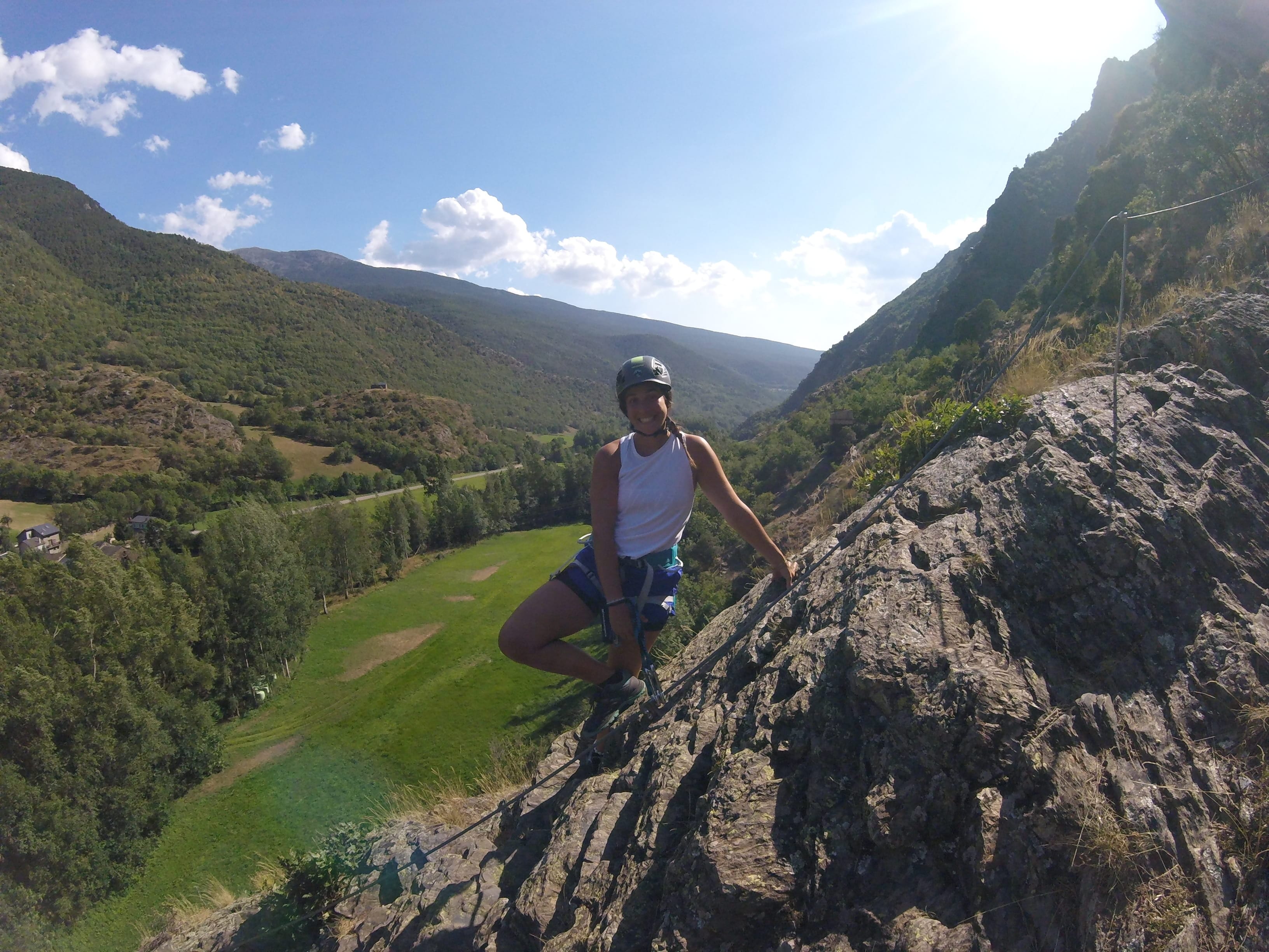 Participante en un tramo rocoso de la vía ferrata Salt de Botanal, asegurada al cable de seguridad con vistas panorámicas del valle verde de montaña