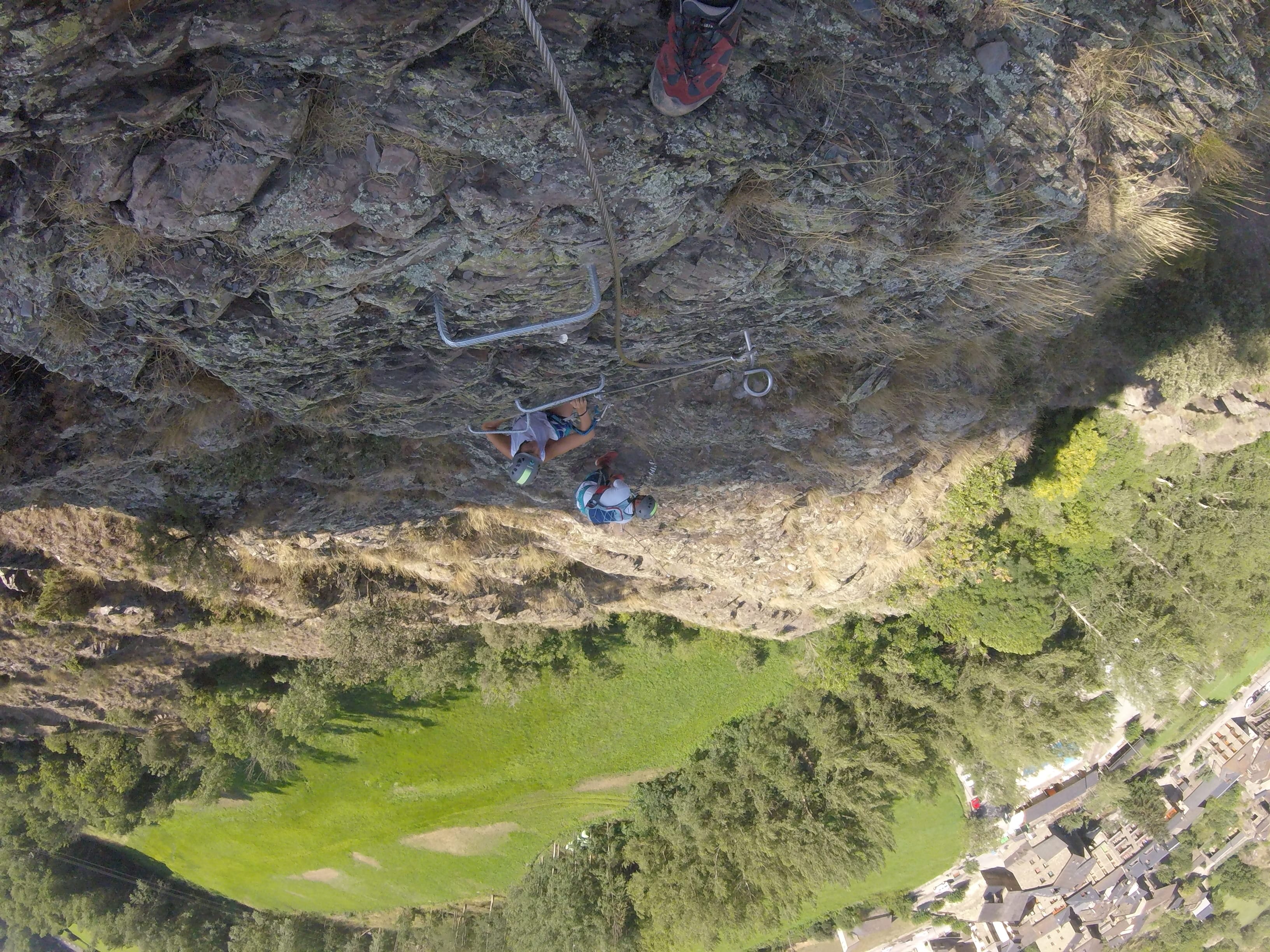Participantes subiendo por un tramo vertical y empinado de la vía ferrata Salt de Botanal, equipados con casco y asegurados al cable de seguridad sobre el valle verde