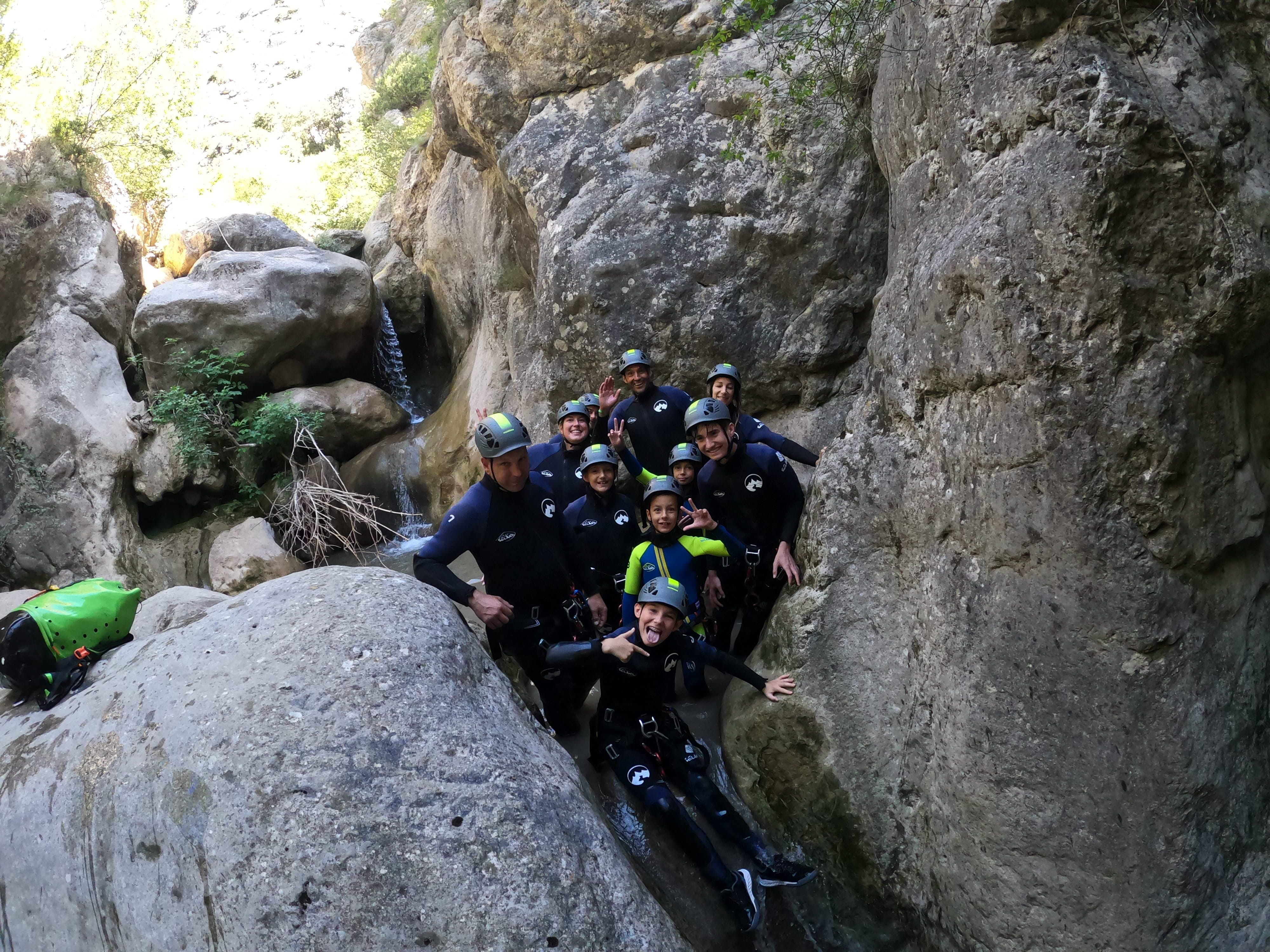 Group of adults and children posing together between large rock walls during a canyoning adventure in Barranco de Bóixols