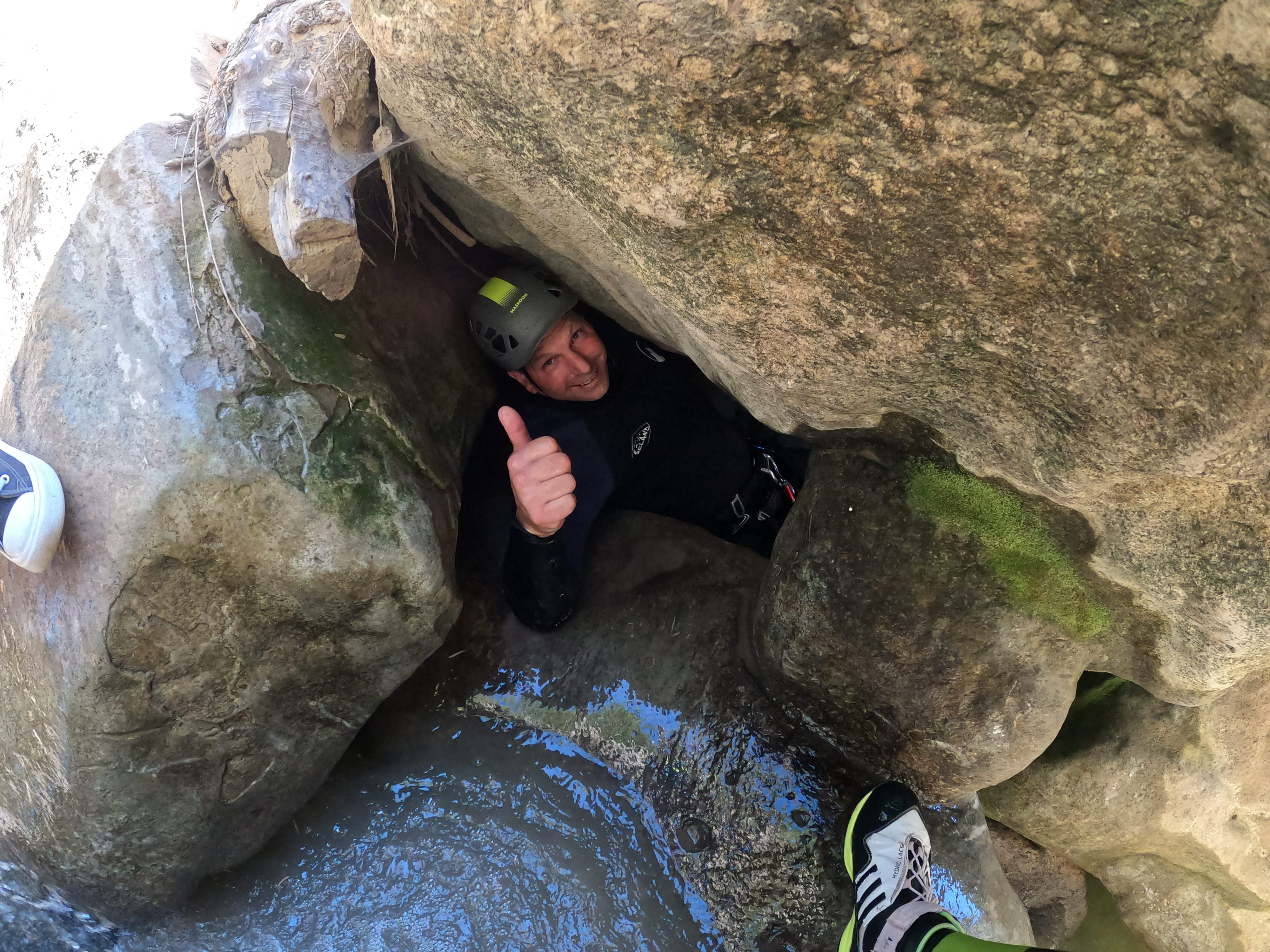 Canyoning participant squeezing through a narrow passage between large rocks and giving a thumbs-up in Barranco de Bóixols