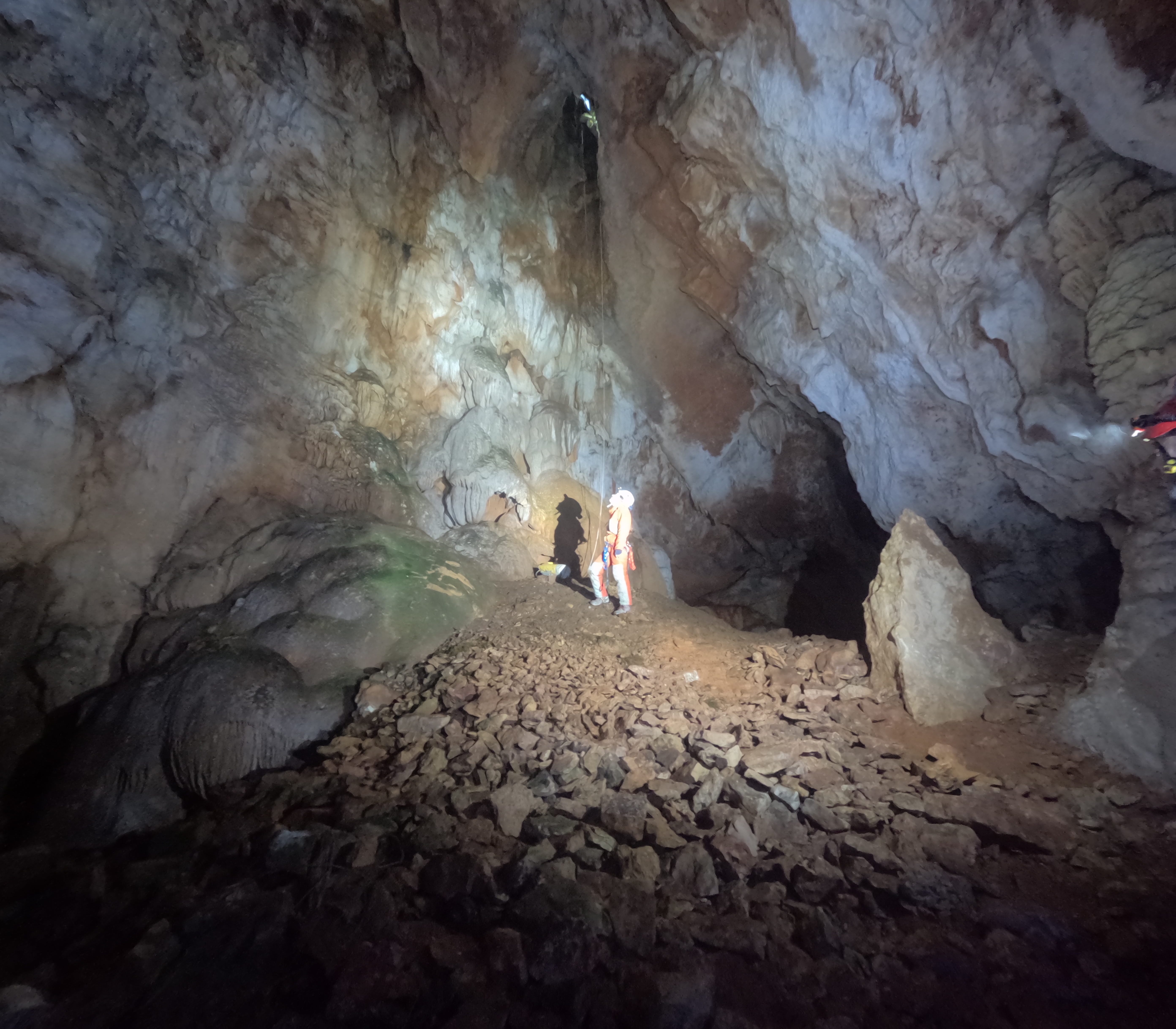 Espeleólogo explorando una inmensa sala subterránea con paredes rocosas y coladas en el interior de la Sima Forat dels Diners
