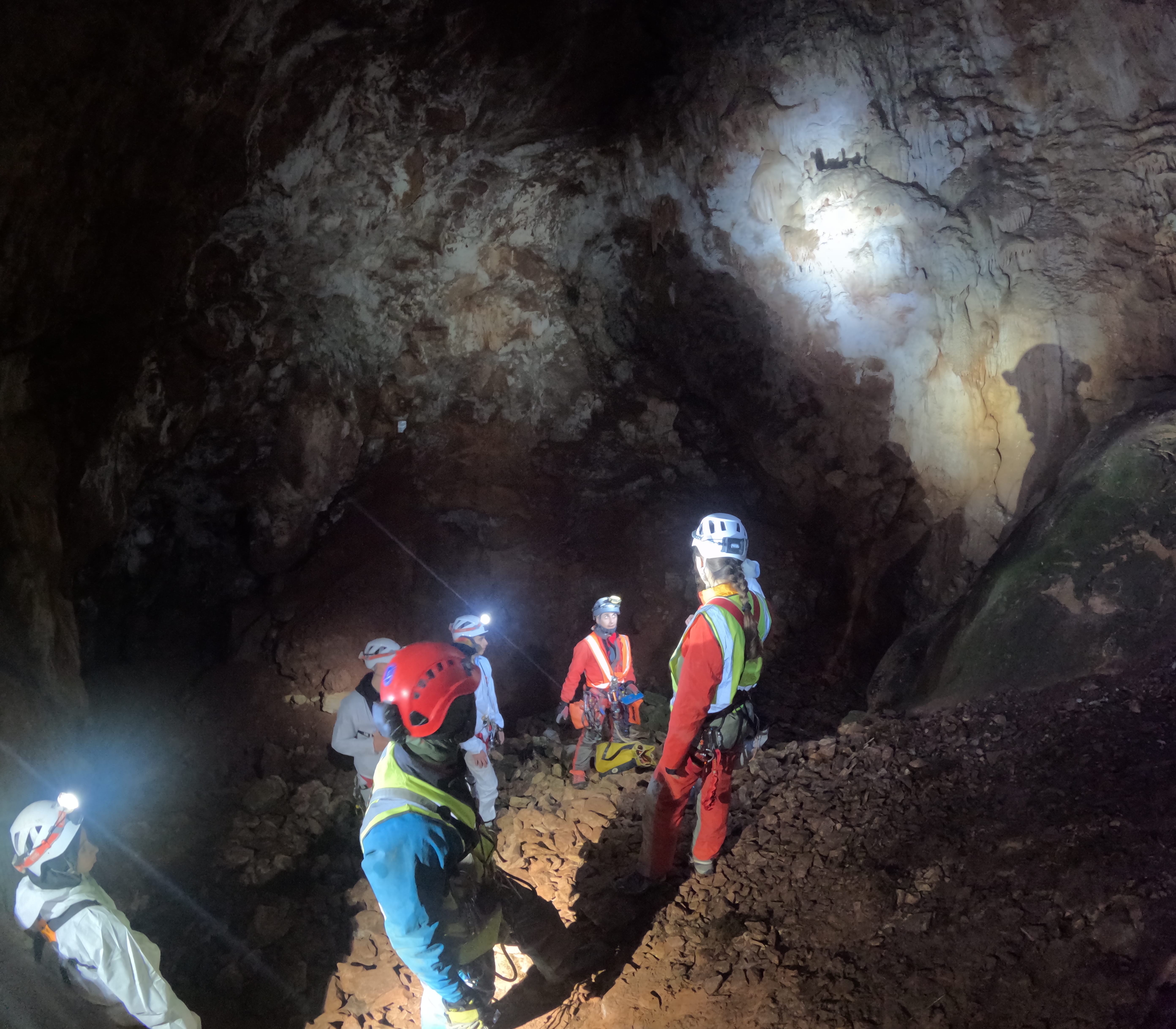 Grupo de espeleólogos explorando una gran sala subterránea iluminada por los frontales en el interior de la Sima Forat dels Diners