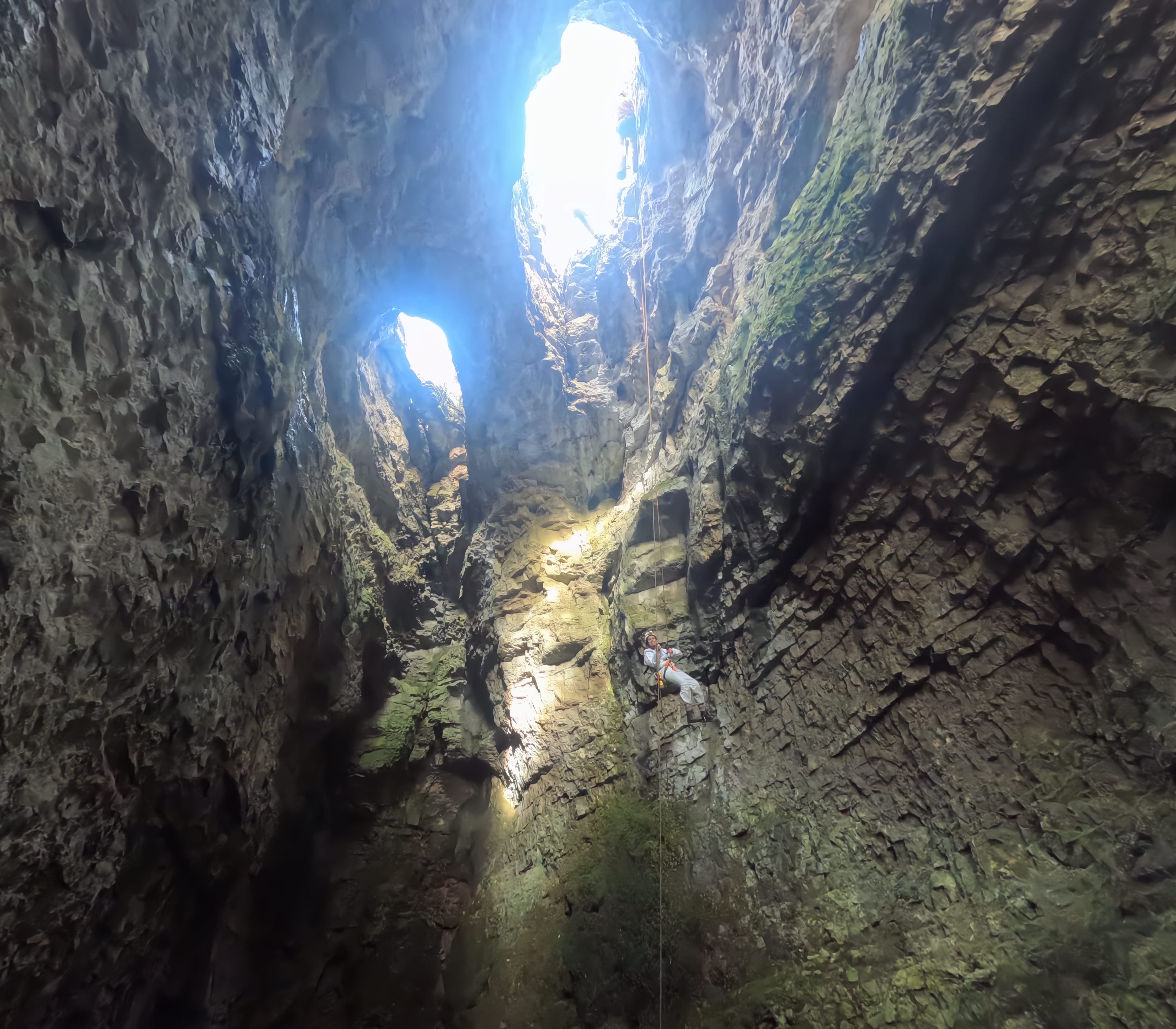 Espeleólogo descendiendo con cuerda por el espectacular pozo vertical de la Sima Forat dels Diners, iluminado por la luz natural que entra desde arriba