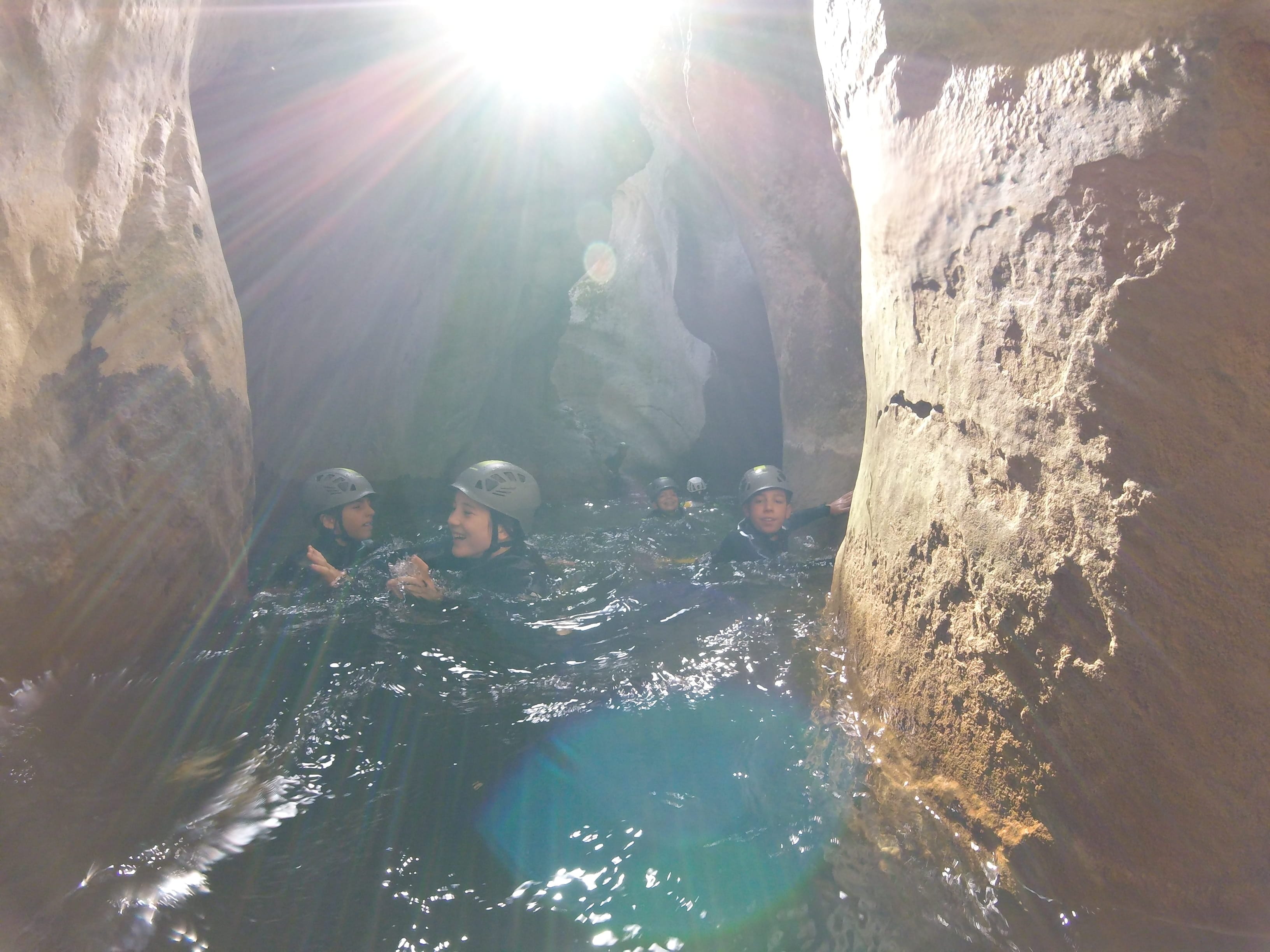 Canyoning group swimming through a narrow sunlit gorge in Barranc de Viu de Llevata