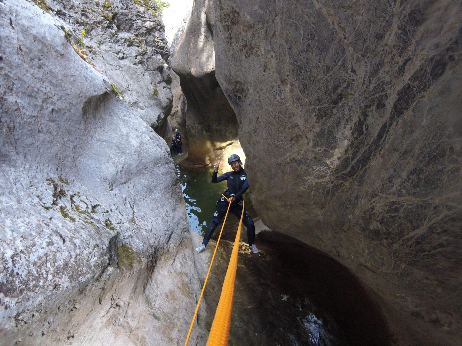 Canyoning participant rappelling through a narrow rock corridor above a natural pool in Barranc de Viu de Llevata