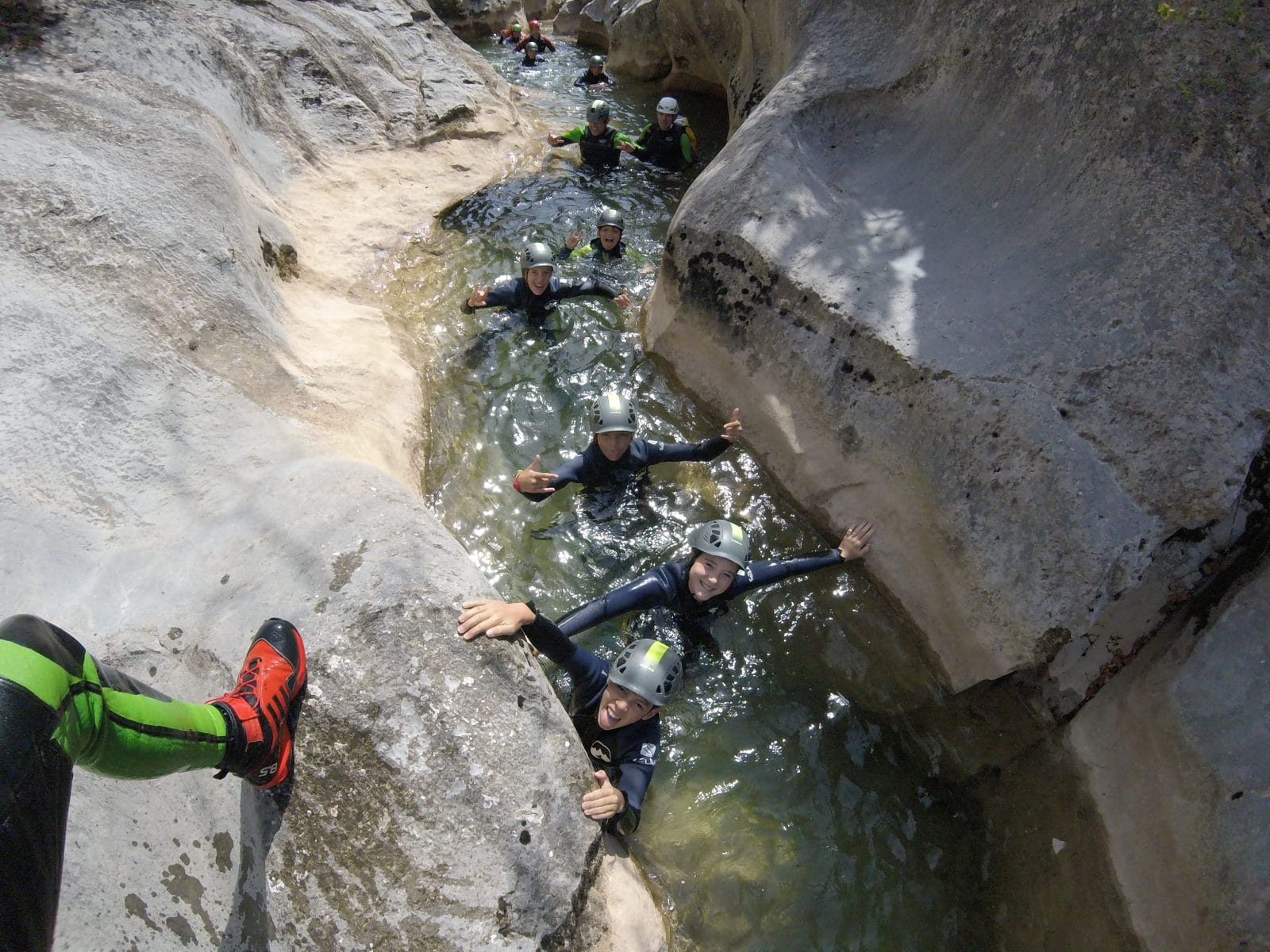 Group canyoning through a narrow water-filled passage between smooth rock walls in Barranc de Viu de Llevata