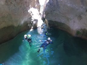 Swimming through a deep turquoise pool between rock walls in Peonera Canyon
