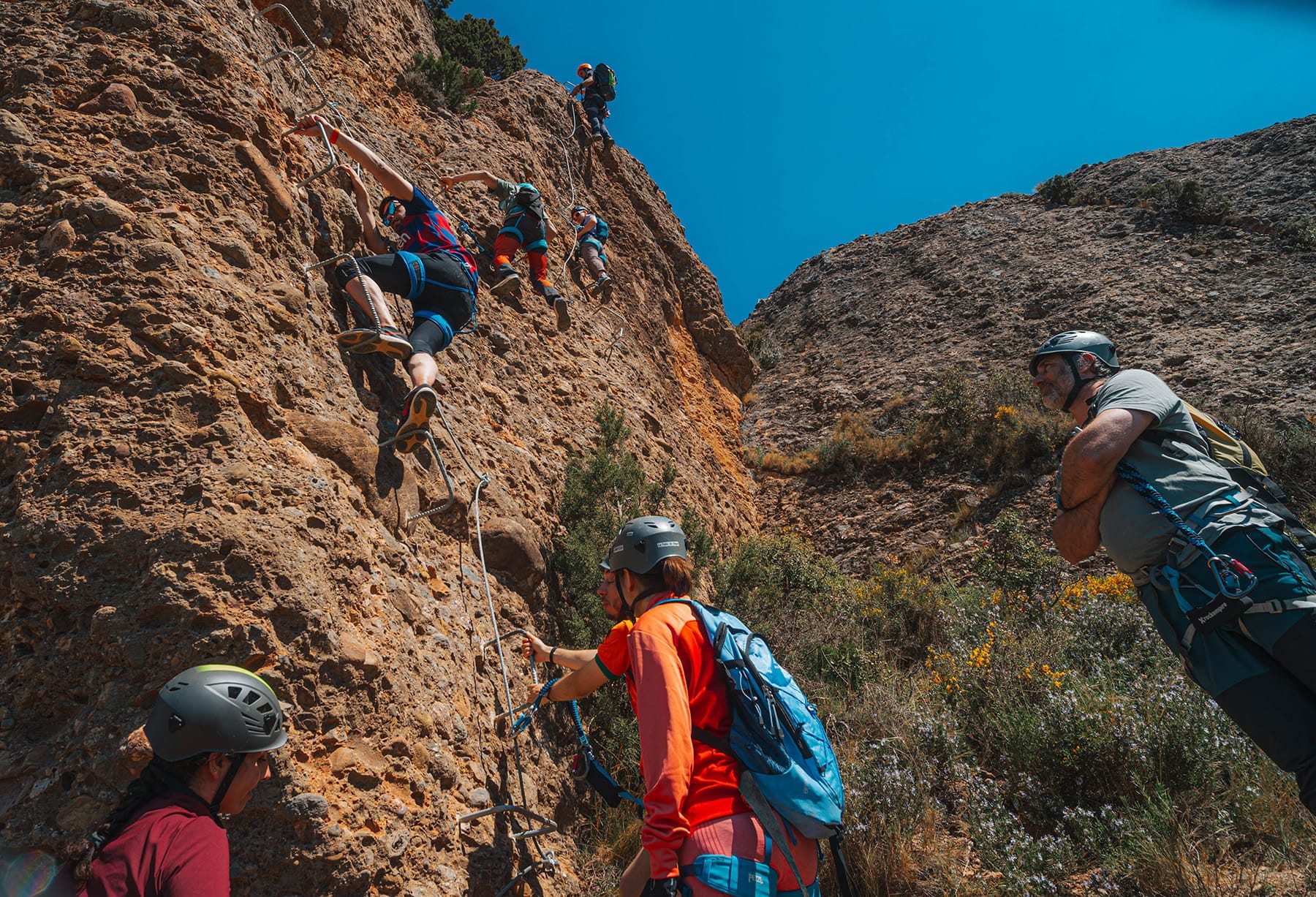 Group of climbers ascending a steep section of the Vía Ferrata Roca Foradada using metal rungs and safety cables near La Pobla de Segur