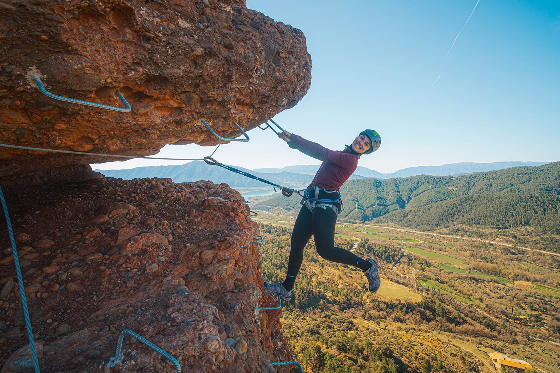 Climber enjoying an exposed overhanging section of the Vía Ferrata Roca Foradada, secured to the safety cable with panoramic views over the valley near La Pobla de Segur