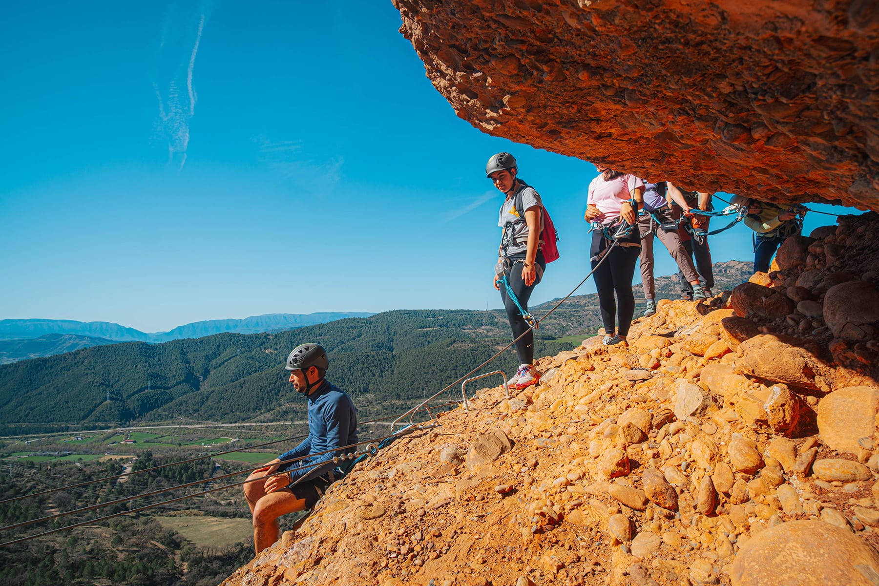 Group of climbers preparing for the cable bridge section of the Vía Ferrata Roca Foradada, secured with helmets and harnesses above the valley near La Pobla de Segur