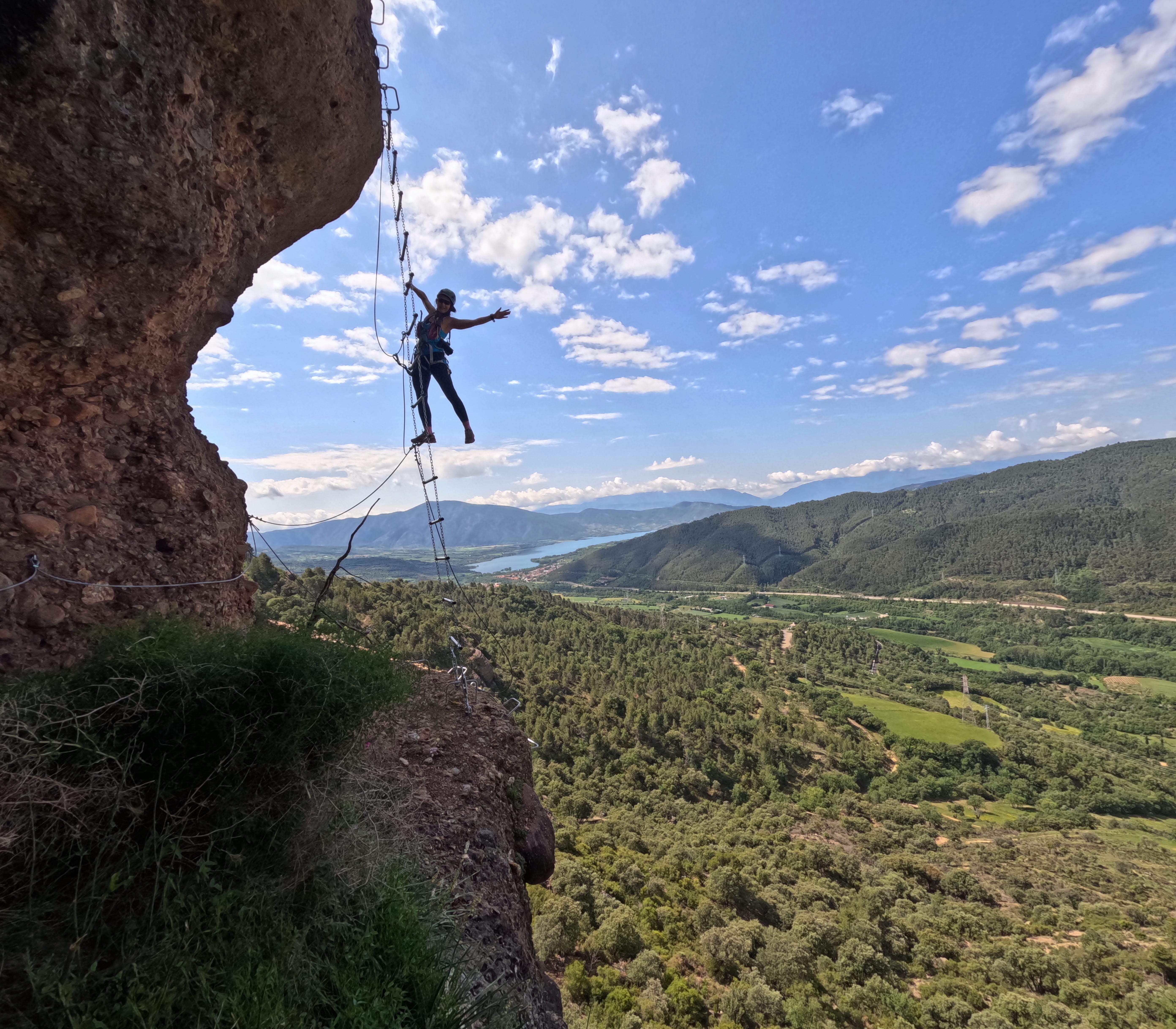 Participante cruzando el puente tibetano de la Vía Ferrata Roca Foradada en La Pobla de Segur, con vistas al embalse de Sant Antoni y al Prepirineo catalán