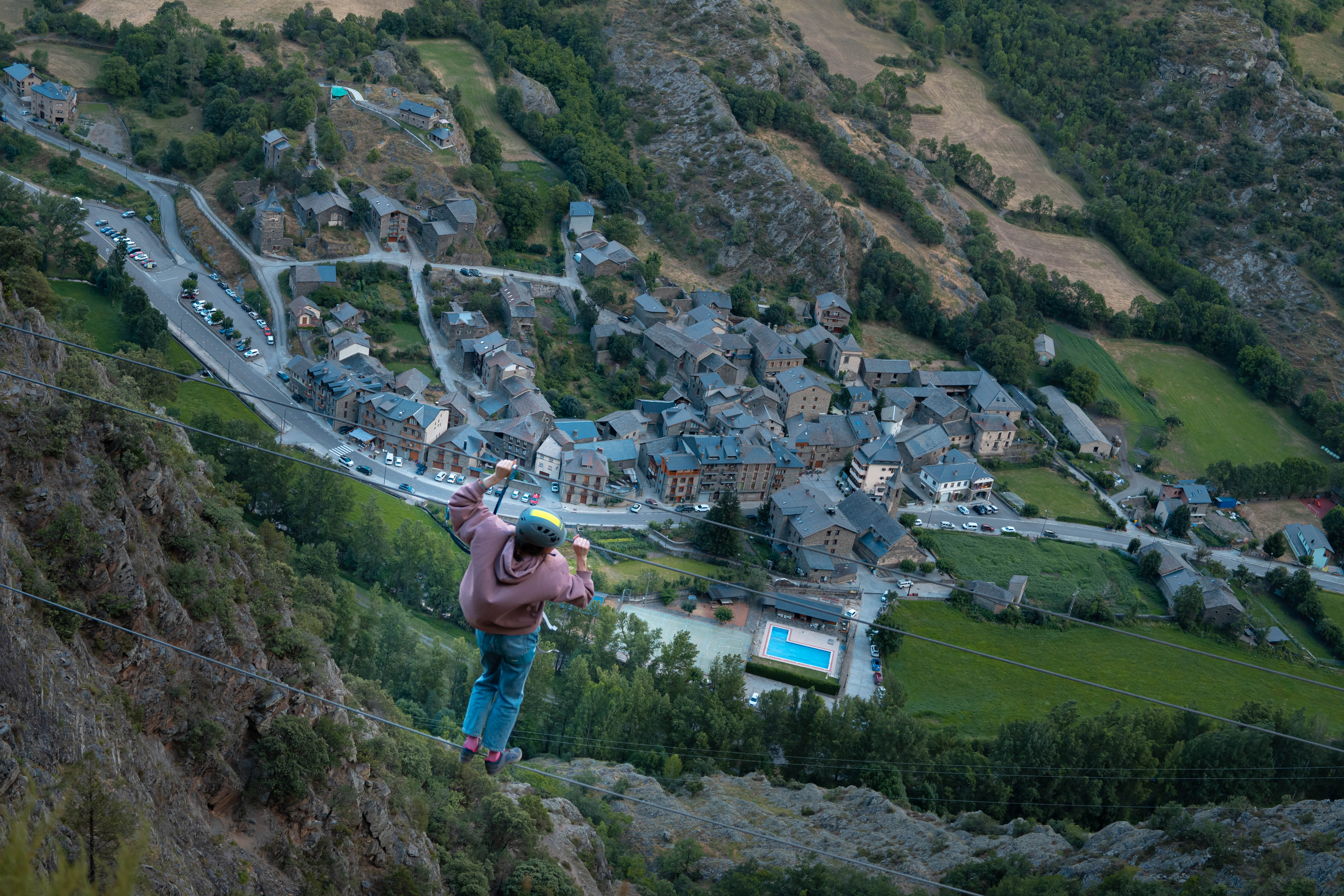 Participante cruzando el puente tibetano de la Vía Ferrata Salt del Botanal en Alins, con vistas al valle de la Vall Ferrera y al Pirineo