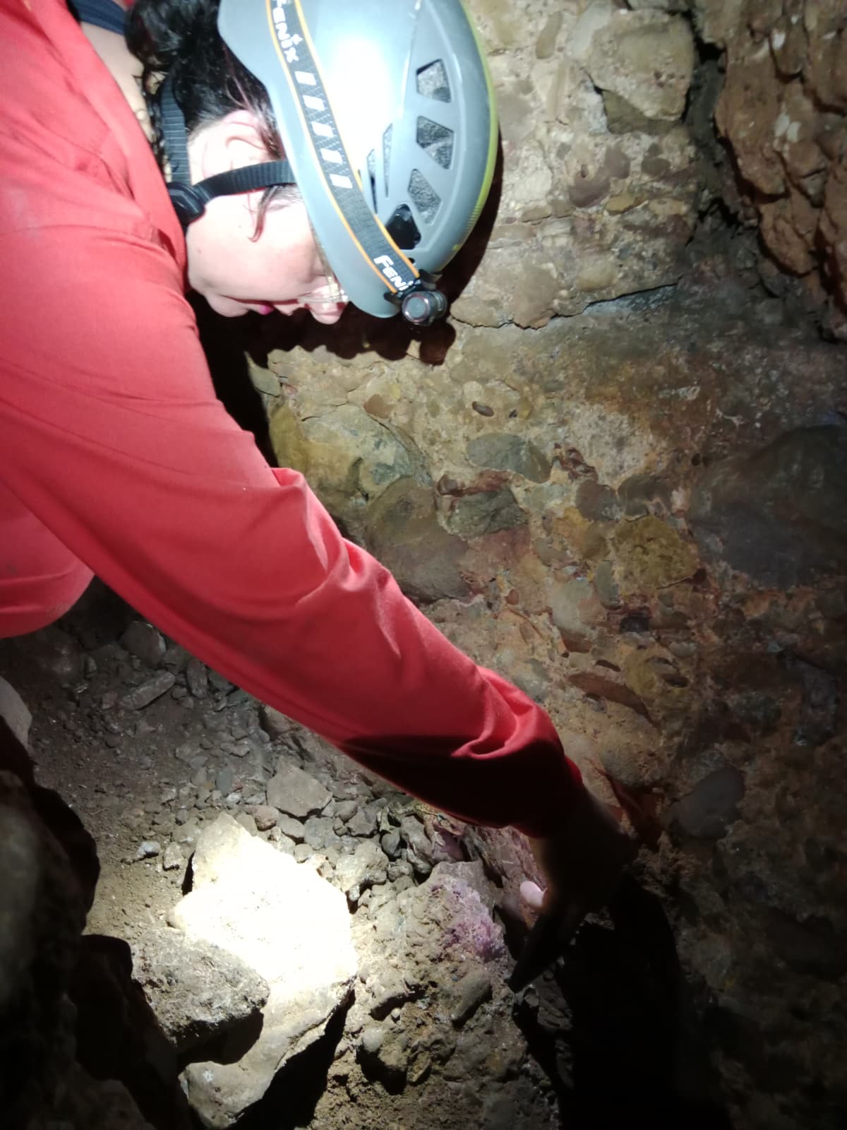 Caver examining the rocky wall inside Cueva Forat la Bou wearing a helmet and headlamp