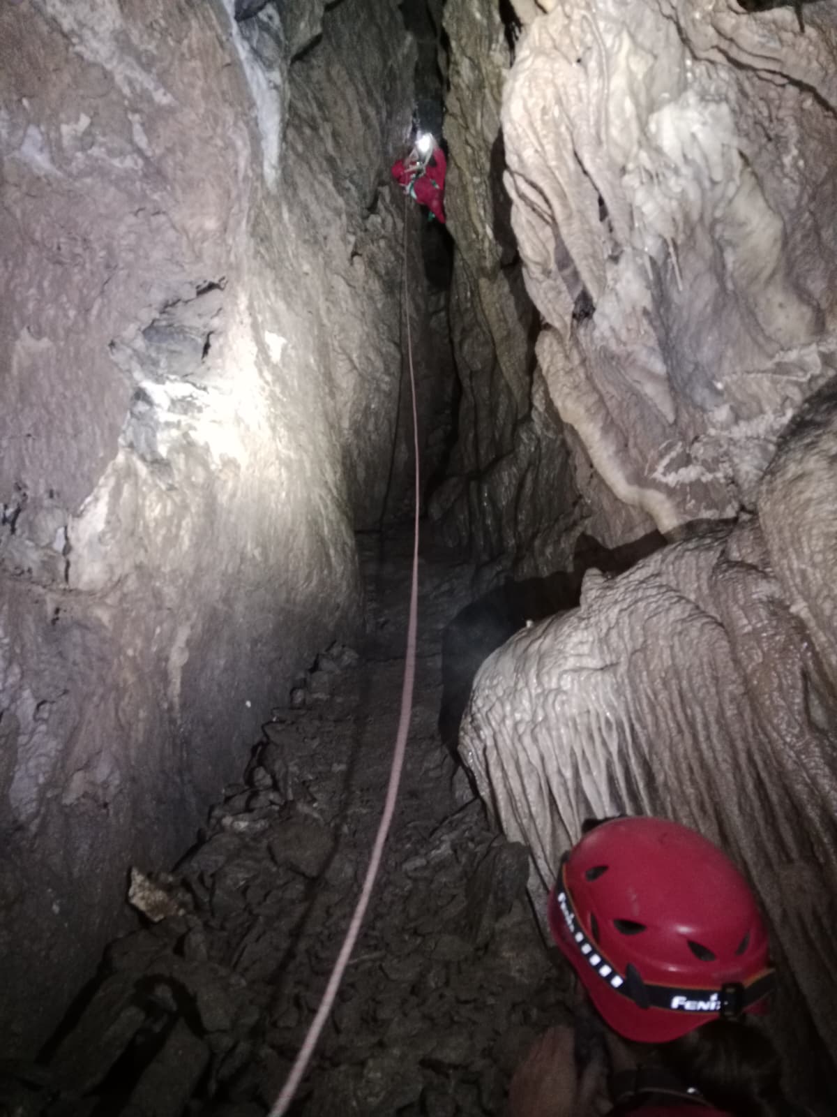 Caver ascending a rope through a narrow vertical passage with flowstone formations inside Sima Tinc ca Tinc