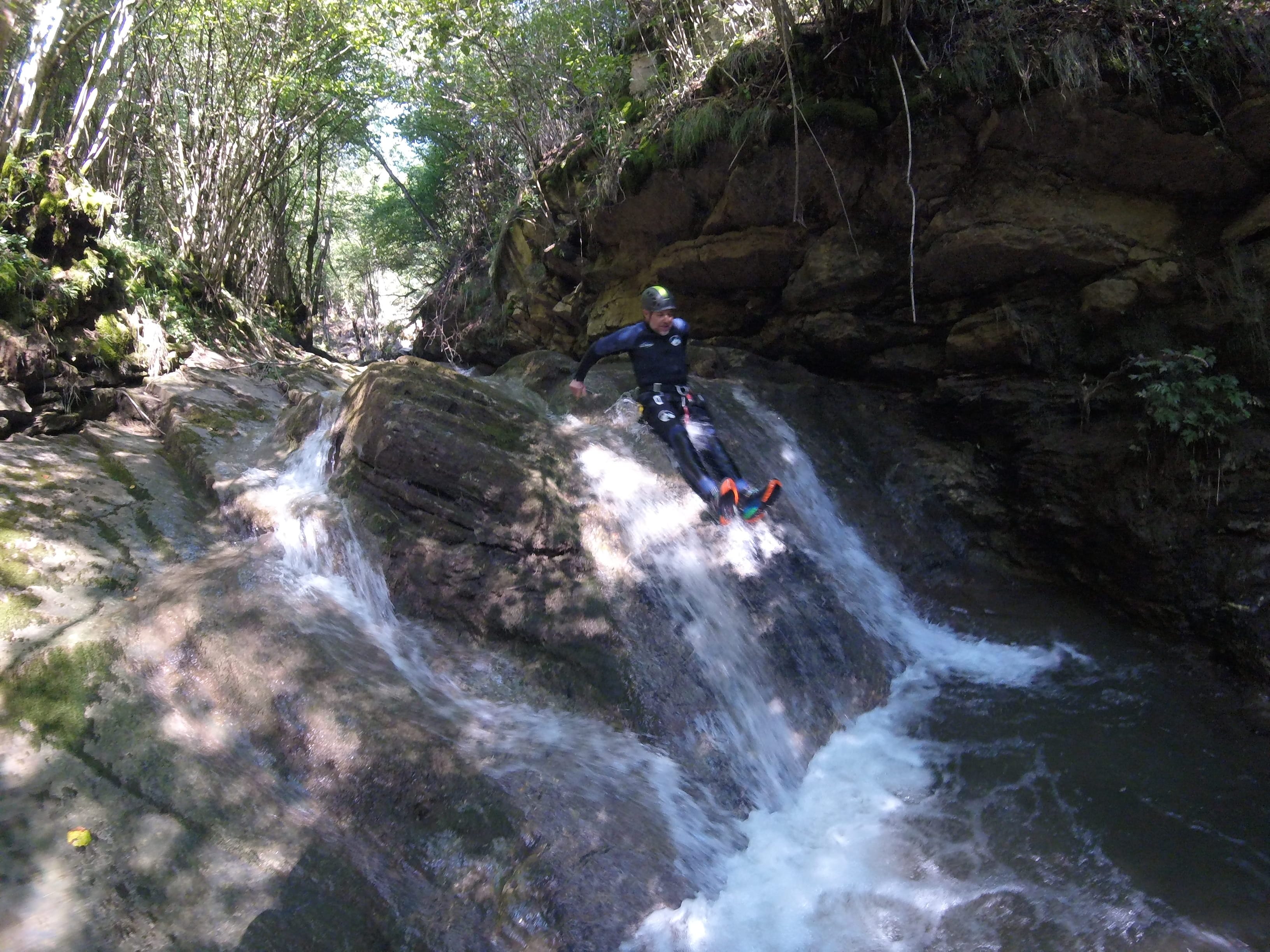 Participant de barranquisme lliscant per una cascada natural de roca envoltada de bosc al Barranc del Pamano