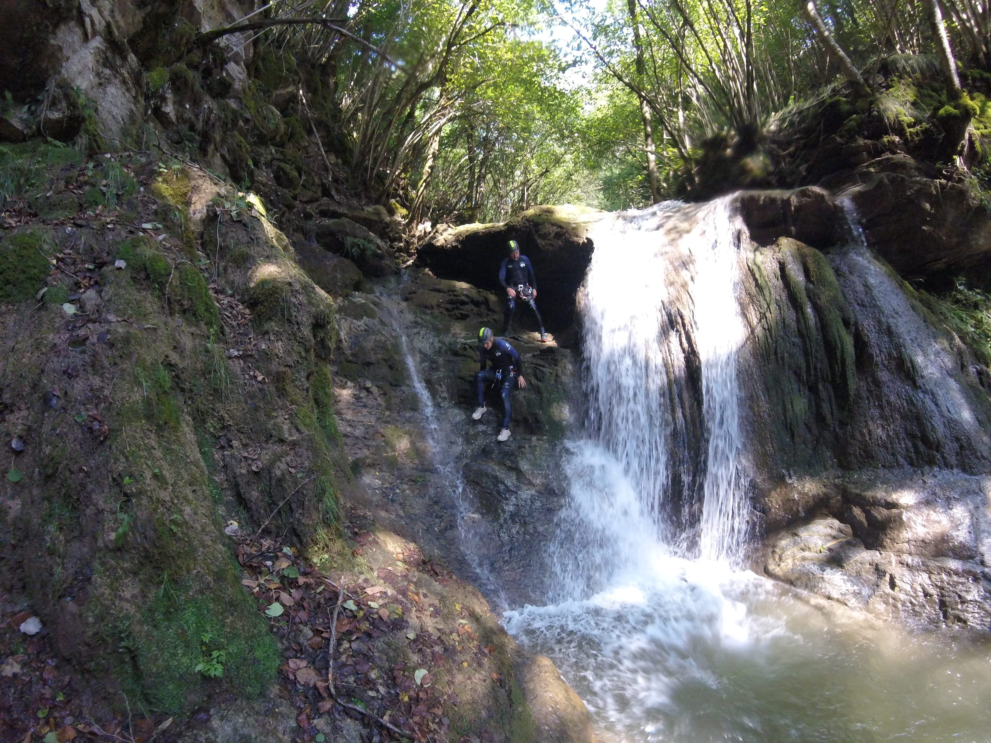 Participants de barranquisme descendint al costat d’una cascada envoltada de bosc al Barranc del Pamano