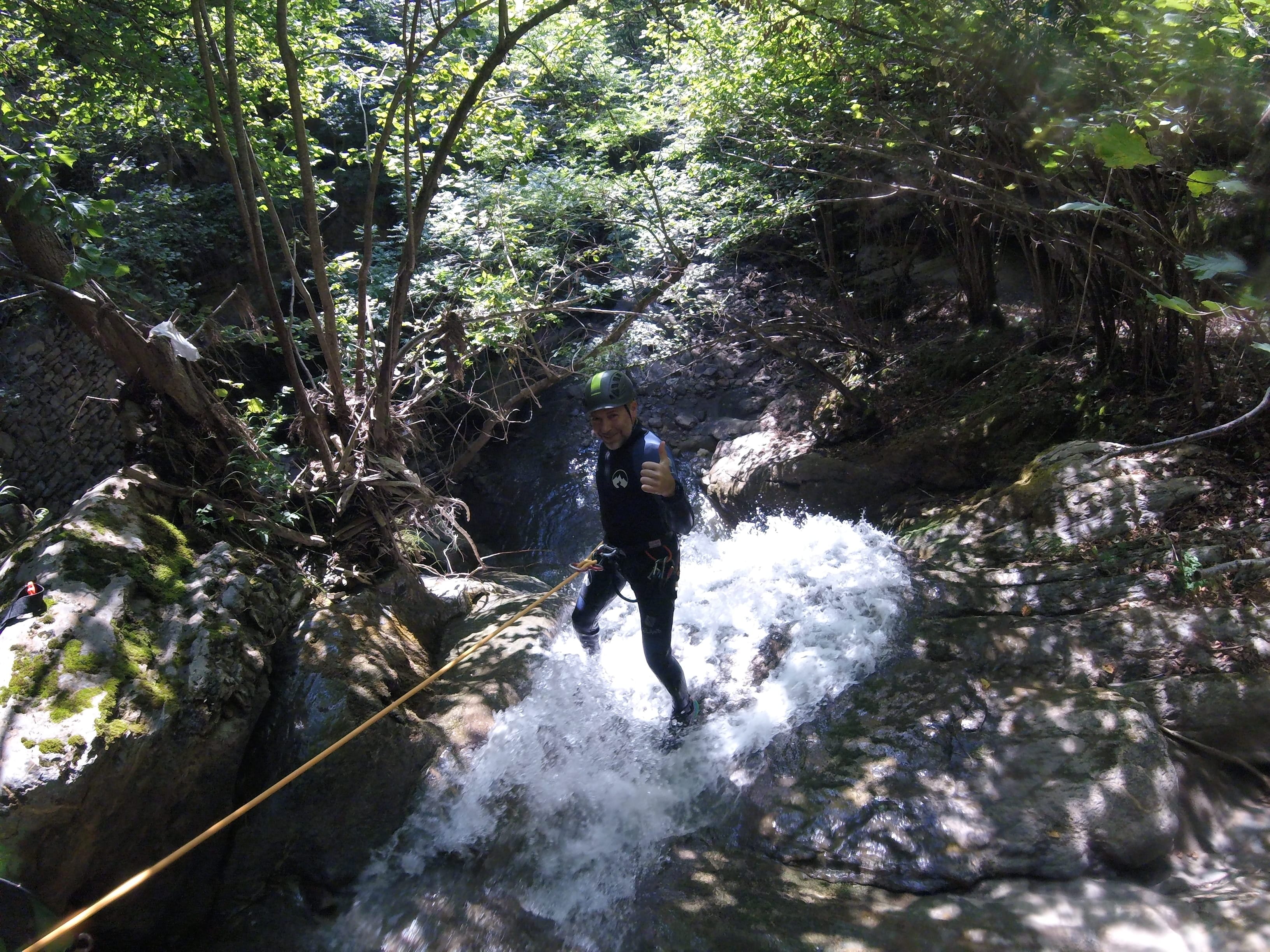 Participant de barranquisme descendint una petita cascada amb corda al bosc del Barranc del Pamano
