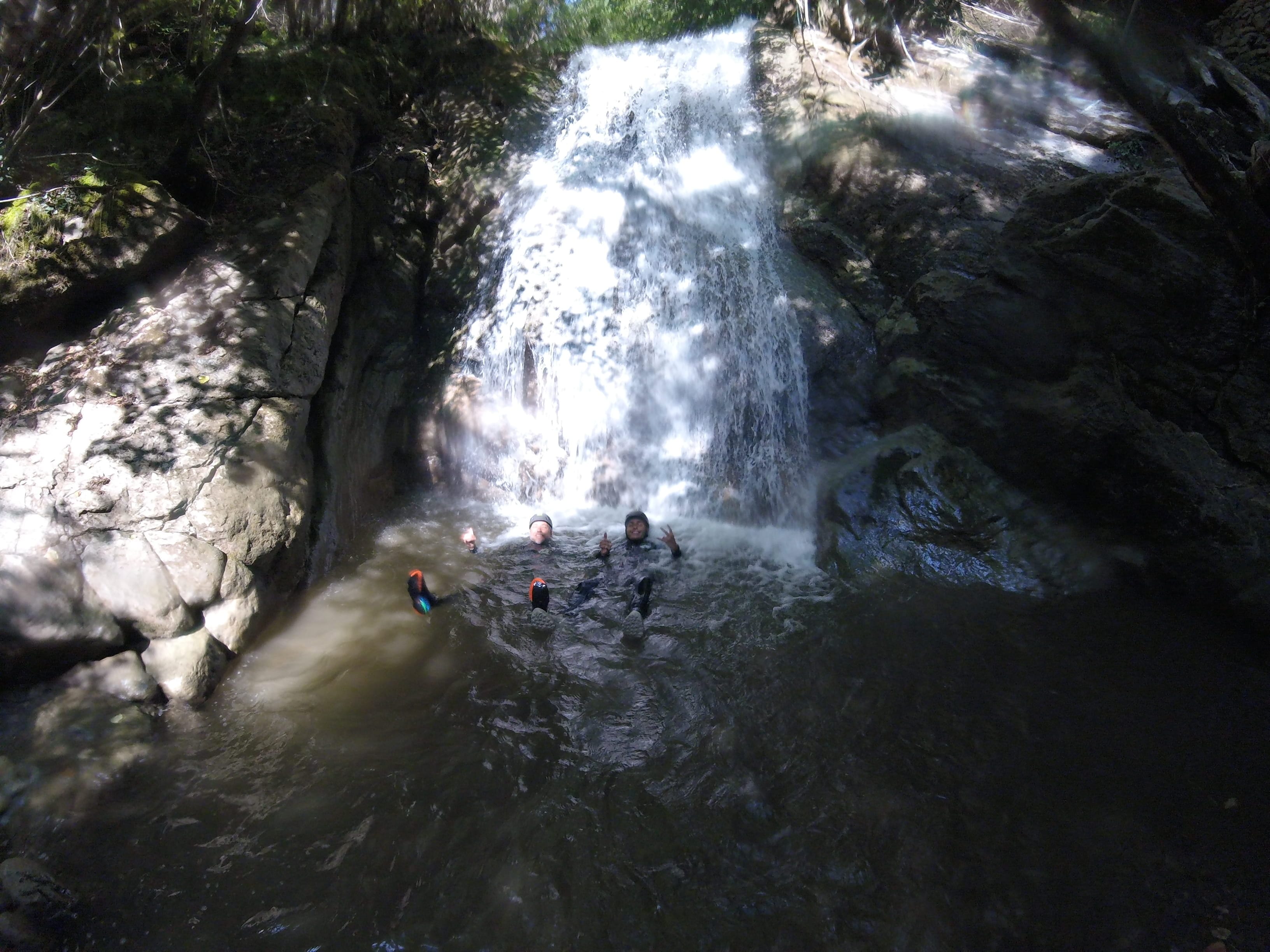 Participants de barranquisme nedant en una poza sota una cascada al bosc del Barranc del Pamano
