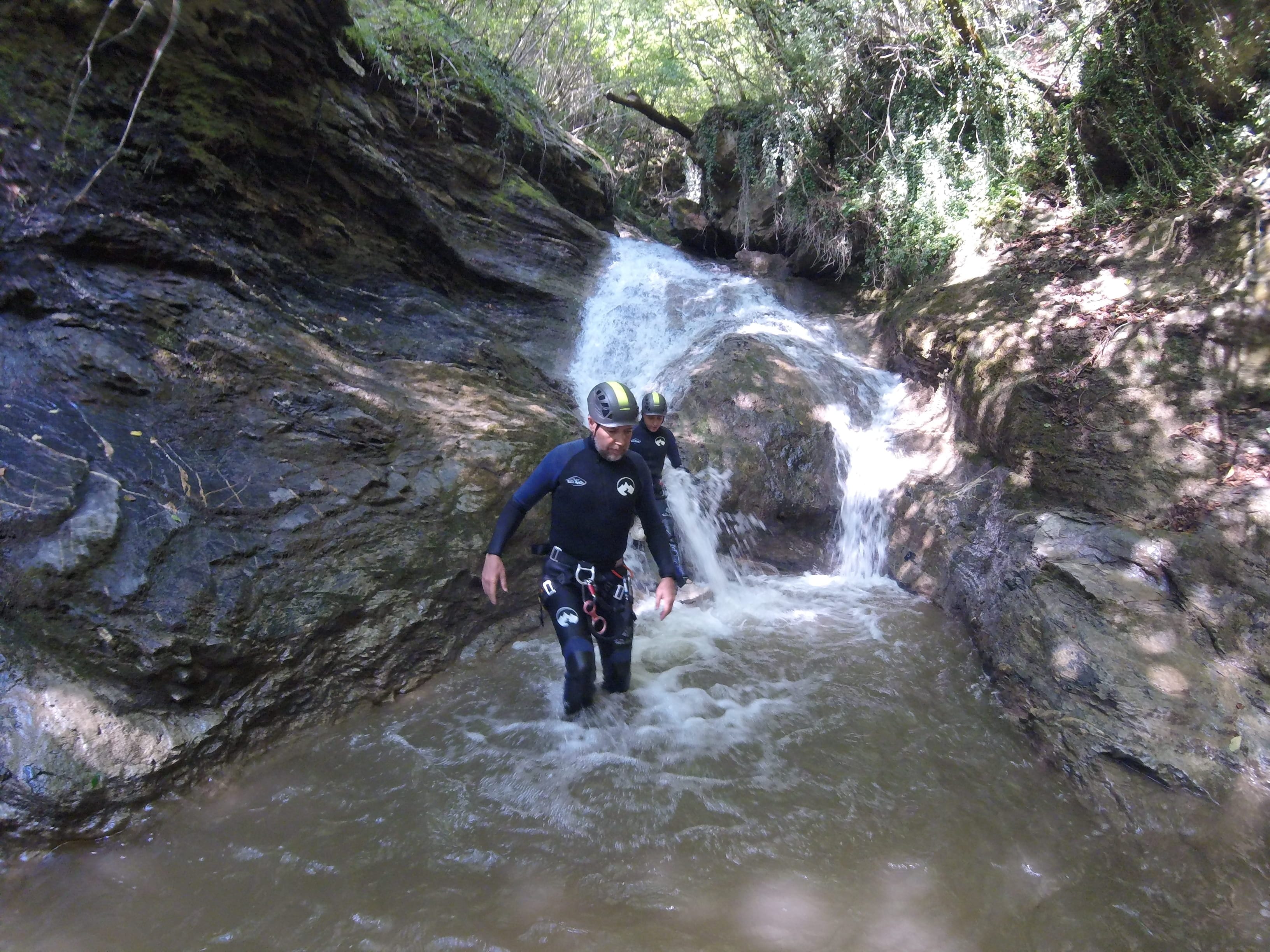 Participants de barranquisme avançant per una cascada rocosa envoltada de bosc al Barranc del Pamano