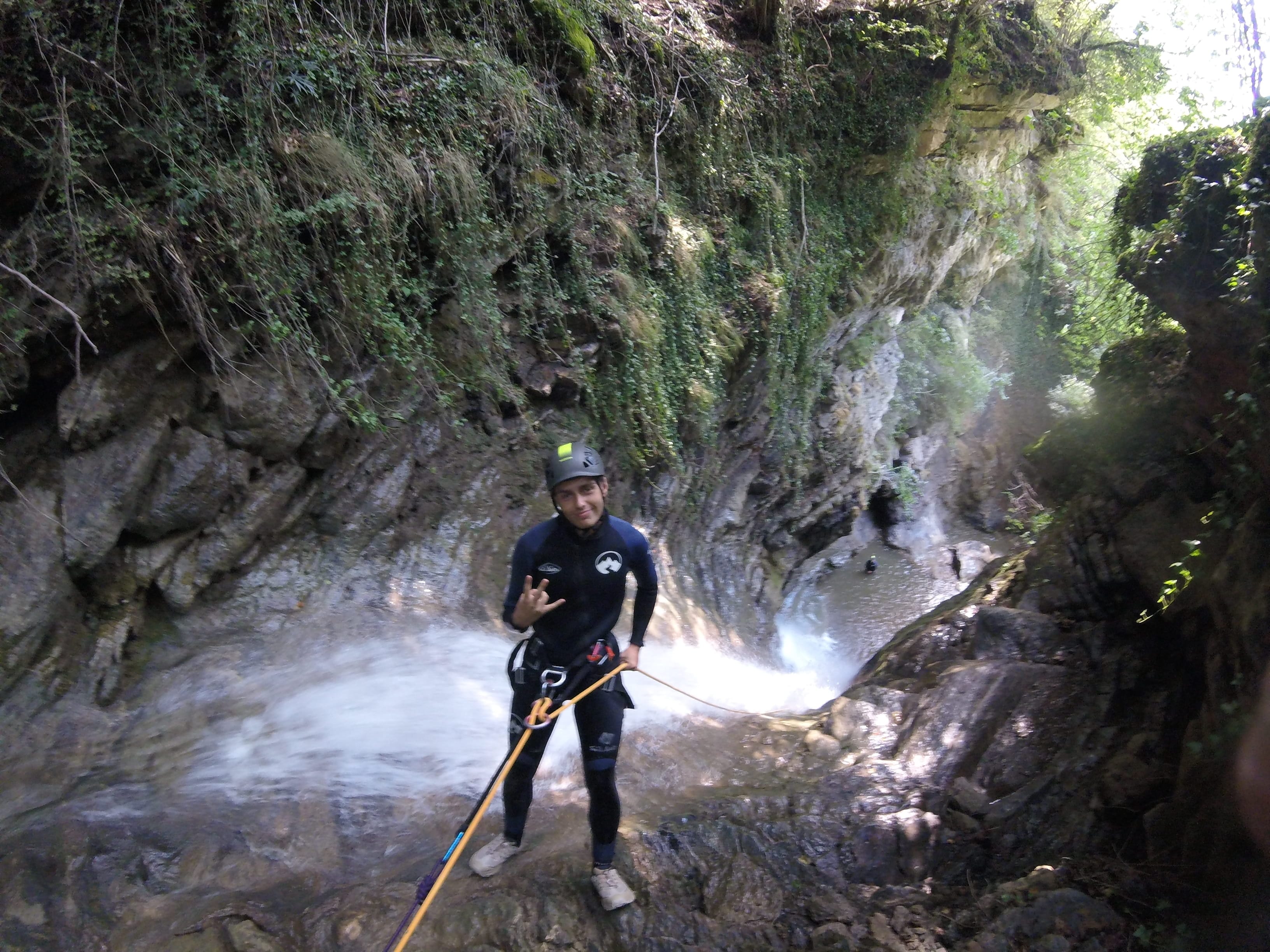 Participant de barranquisme posant amb una corda al costat d’una cascada al bosc del Barranc del Pamano
