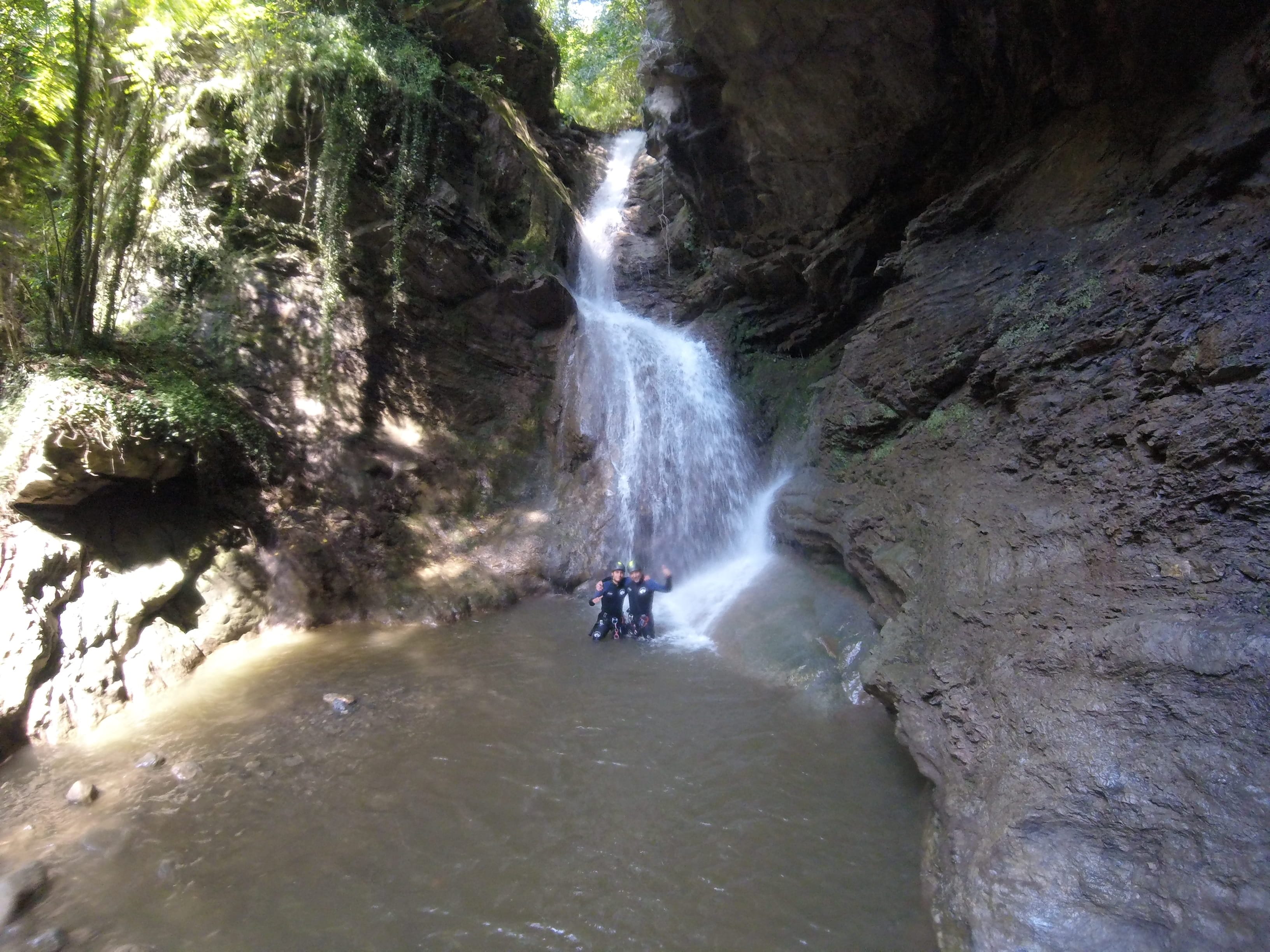 Participants de barranquisme posant en una poza sota una gran cascada al bosc del Barranc del Pamano