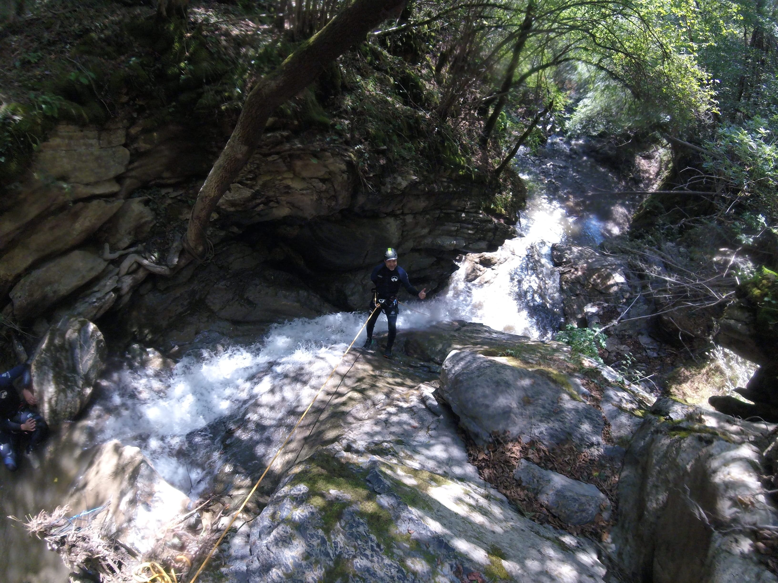 Participant de barranquisme baixant en ràpel per una cascada rocosa envoltada de bosc dens al Barranc del Pamano